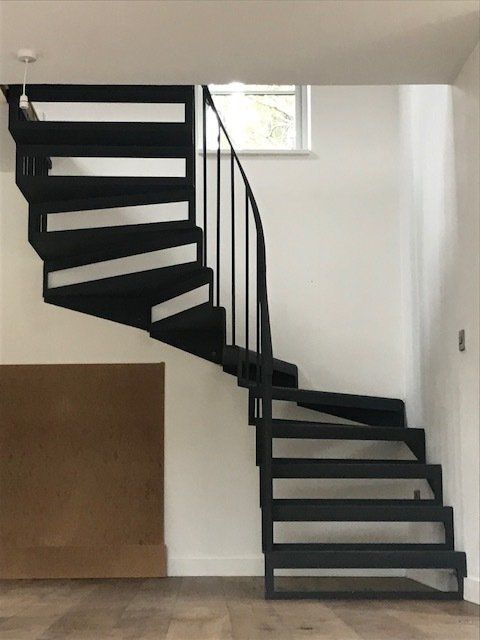 Black spiral staircase in white room, with wooden floor.