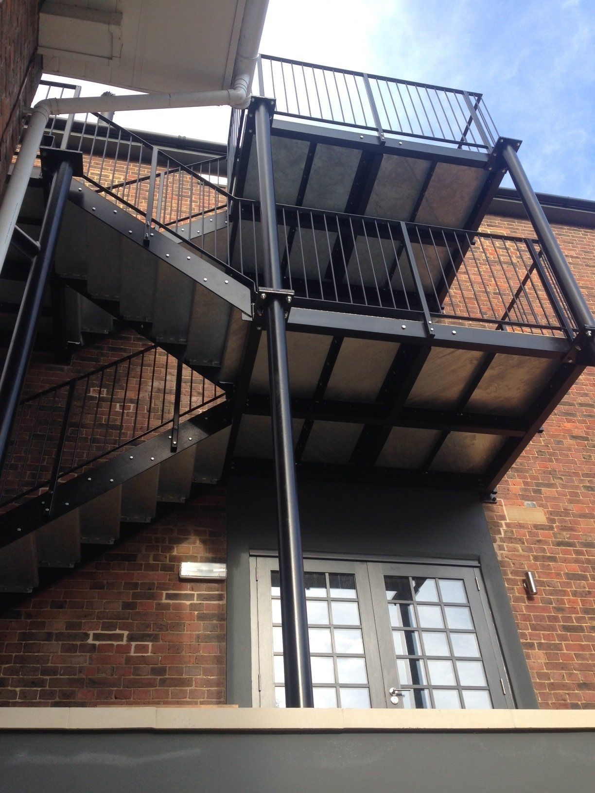 Exterior metal fire escape against a brick building with a white door and blue sky.