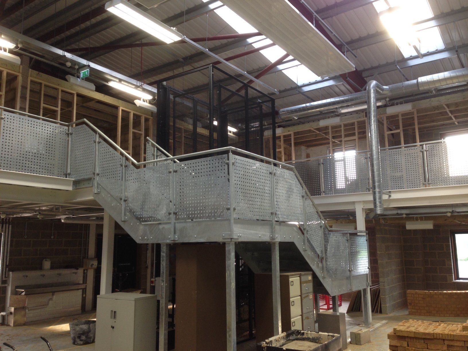 Interior view of unfinished building with metal staircase and lift. Wooden framing visible.
