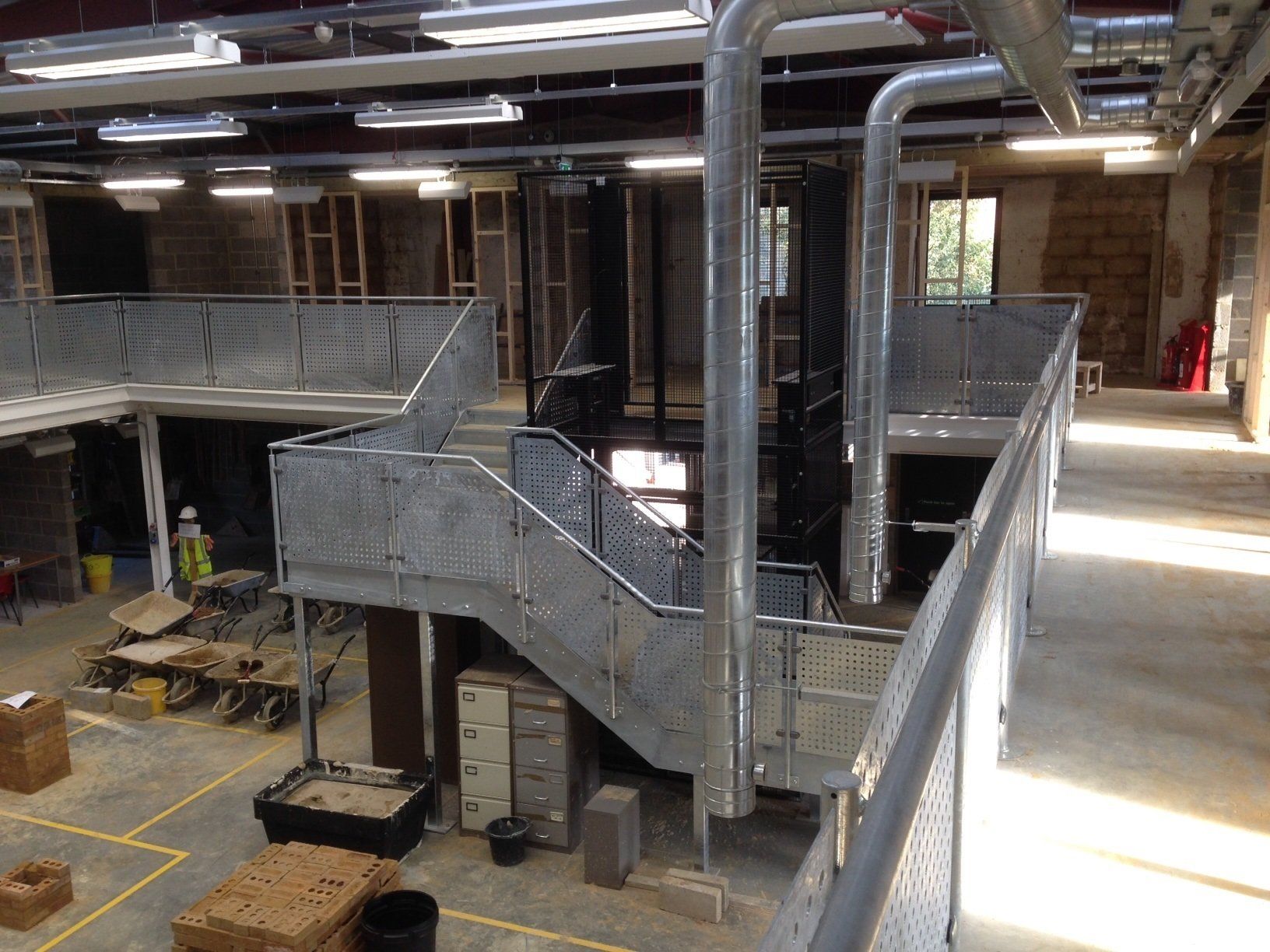 Interior view of a building under construction, featuring metal staircases, scaffolding, and exposed infrastructure.