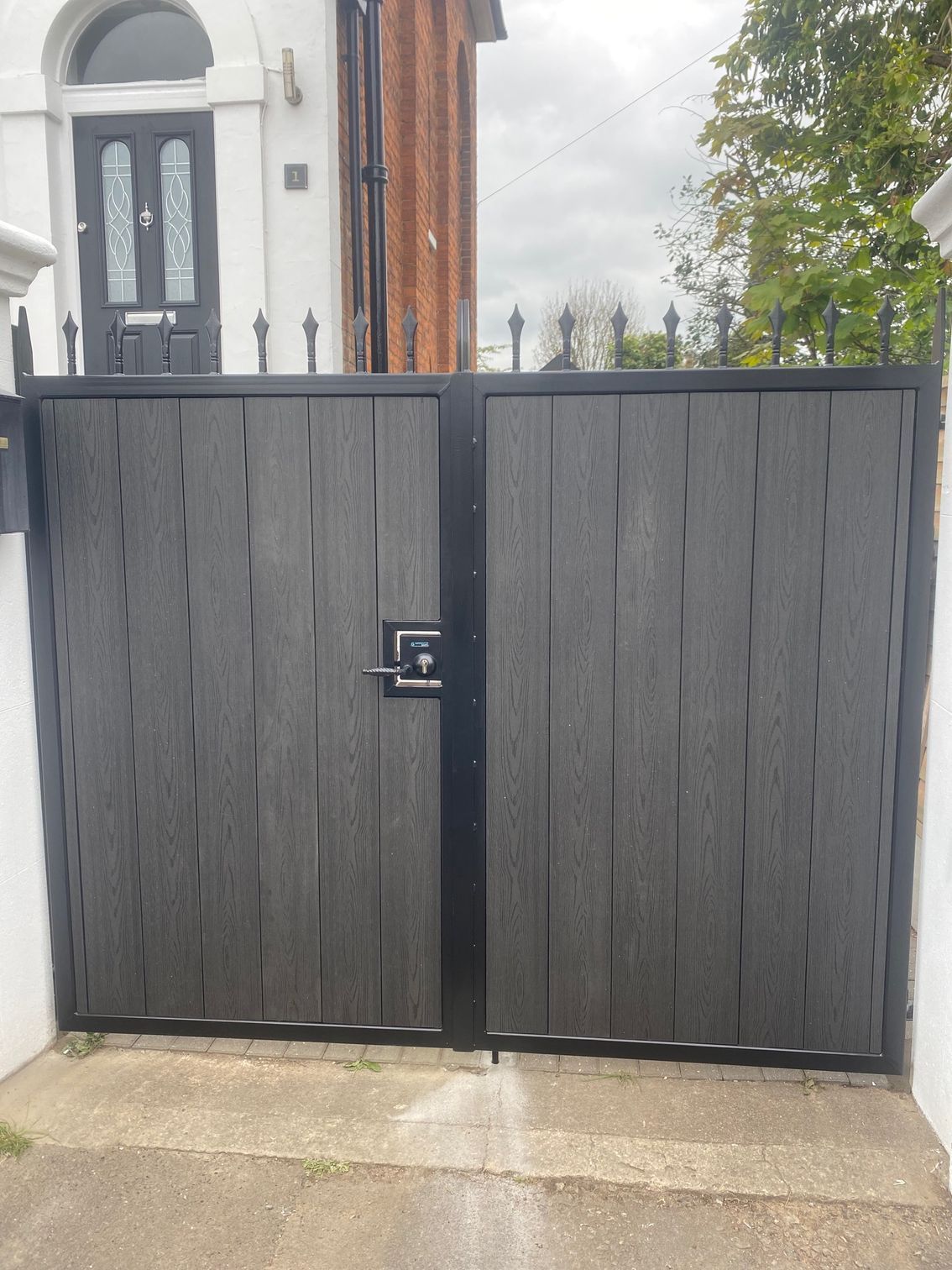 Black wooden gate in front of a house. Vertical wooden planks with black metal frame and lock.
