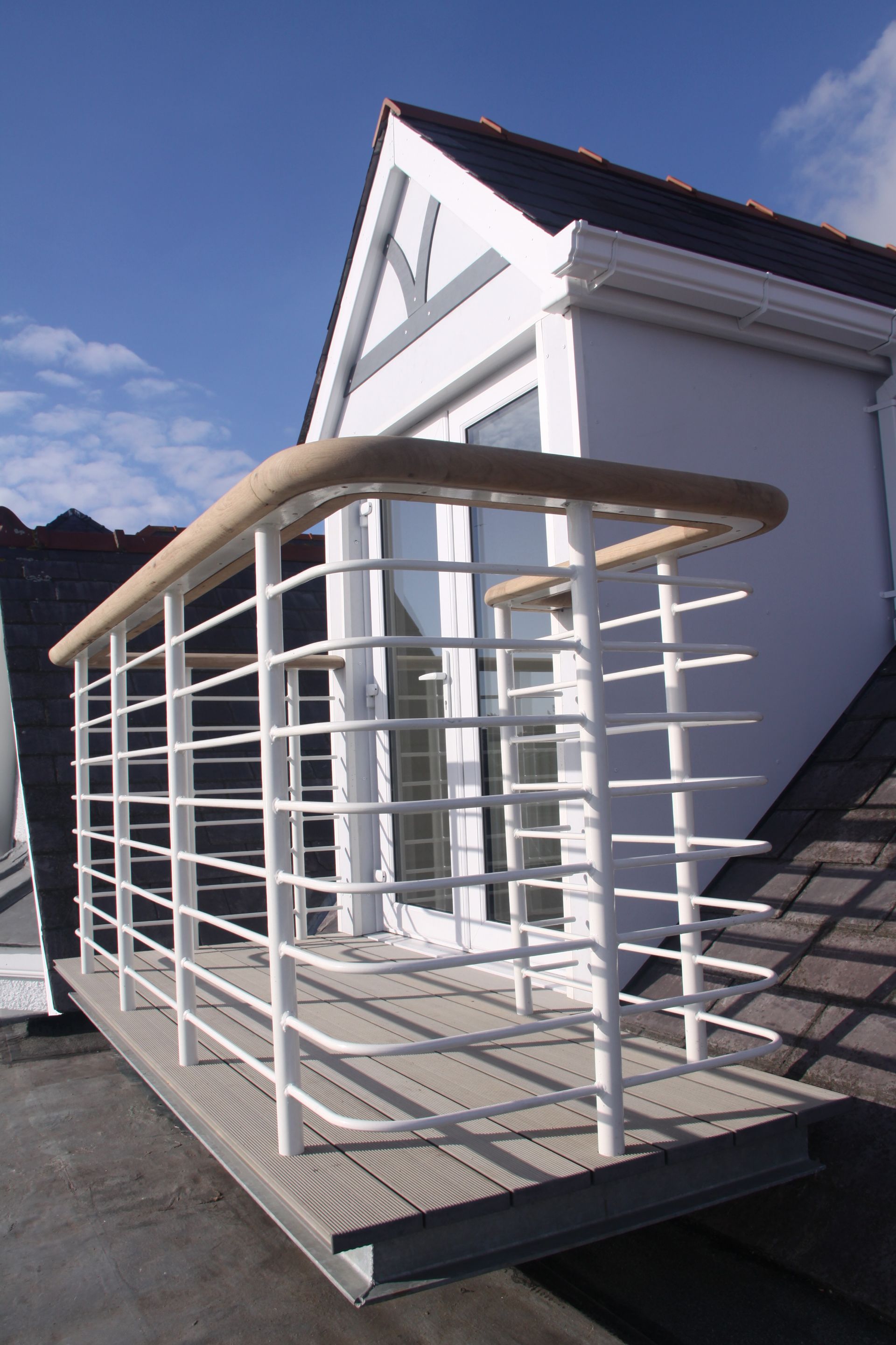 Rooftop balcony with white metal railings and wooden handrail, set against a white dormer window.