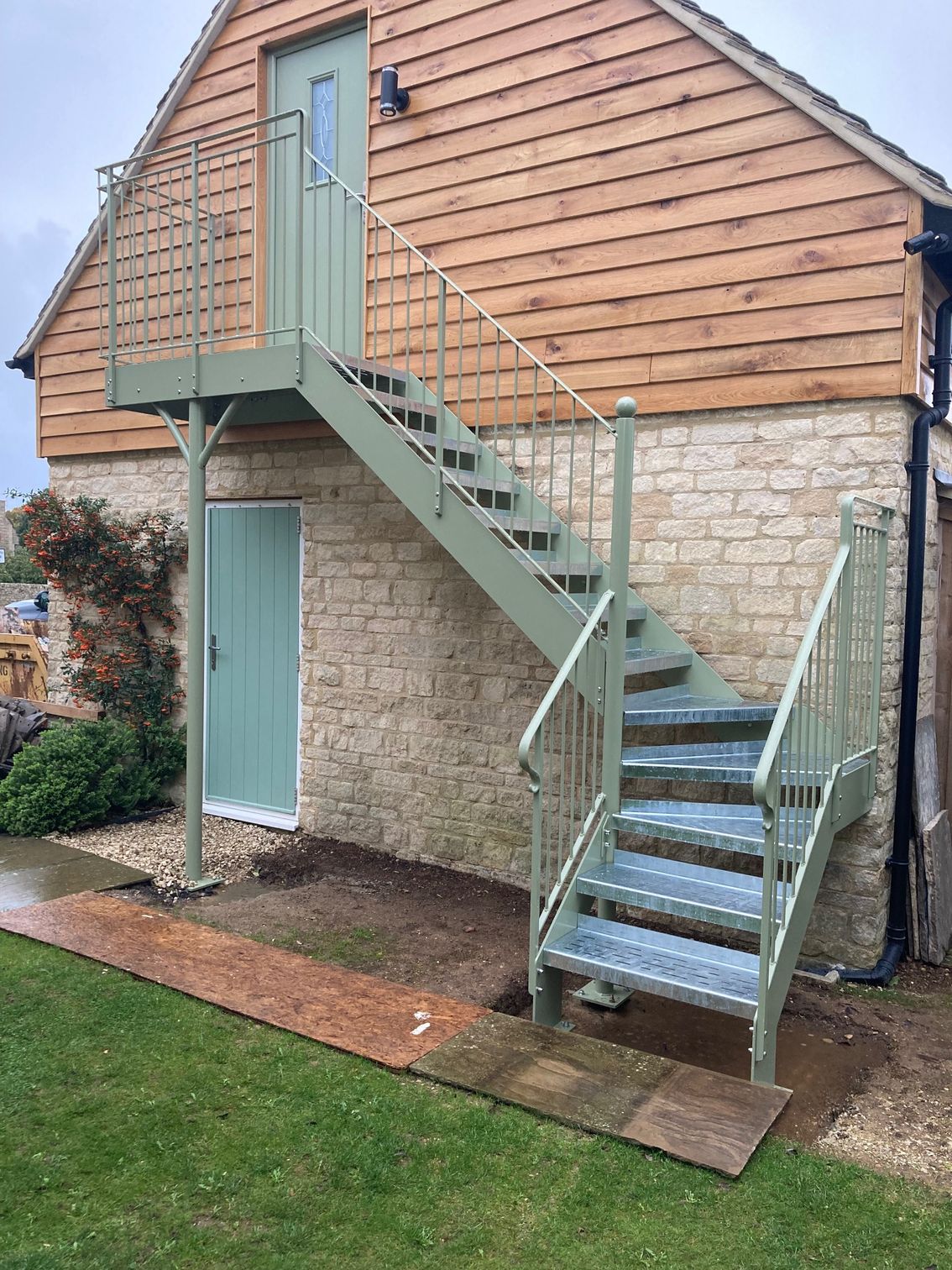 Exterior metal staircase leading to a green door on a building with stone and wood siding.