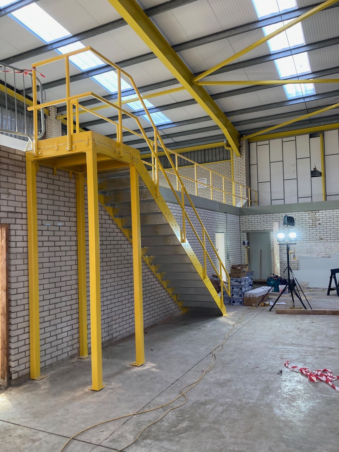 Yellow metal stairs and platform in a warehouse. Brick wall on the left. Concrete floor.