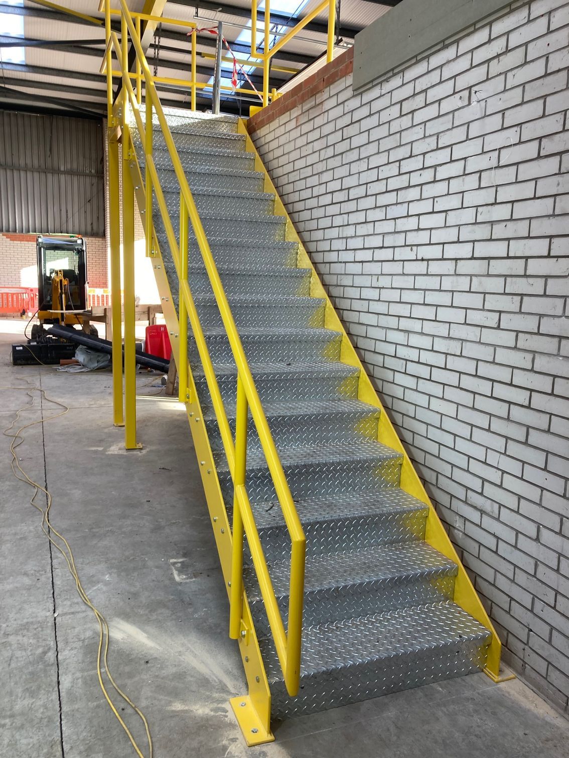 Yellow metal industrial staircase with diamond plate steps against a brick wall.