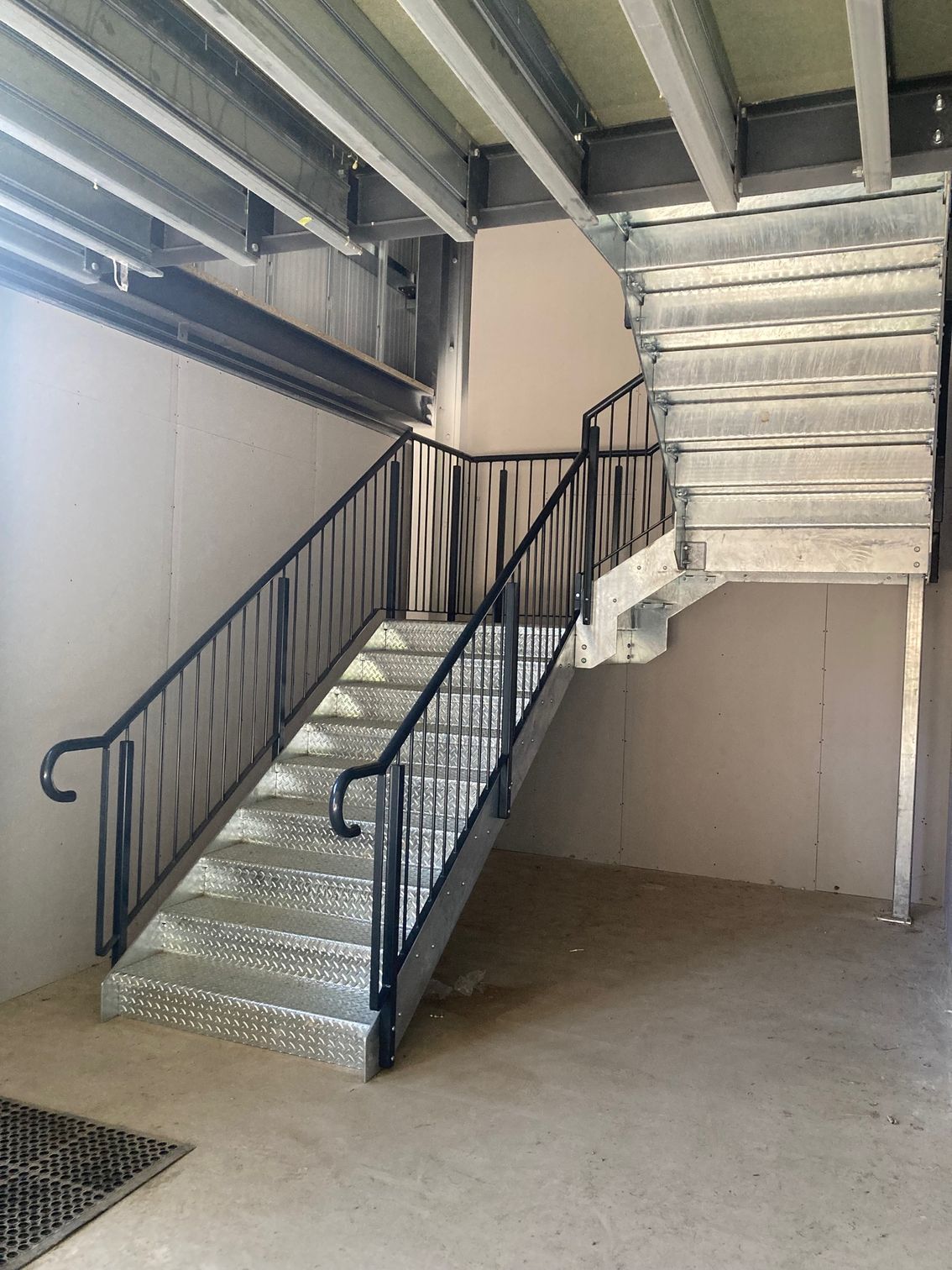 Metal staircase with black handrails and gray treads, leading upward.