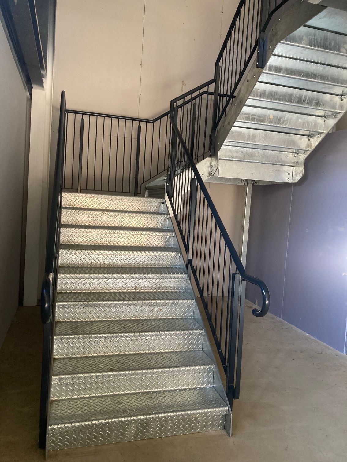 Metal staircase with black handrails and a landing, indoors.