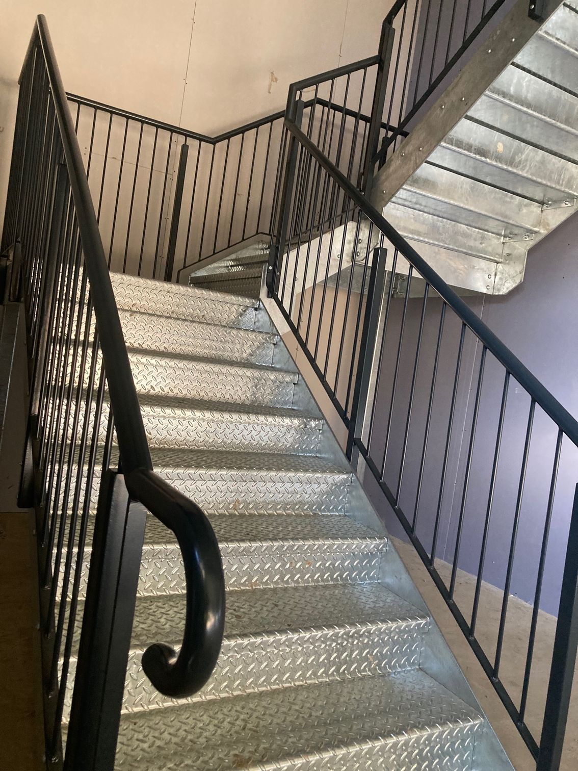 Metal staircase with black handrails and a curved end.