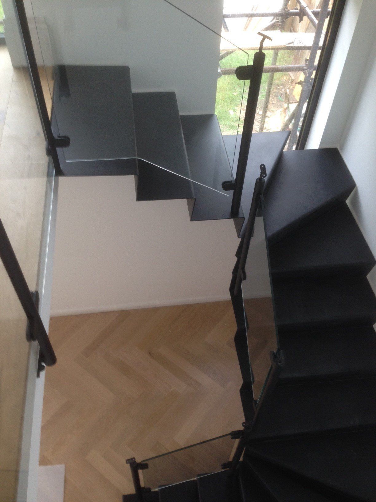 Modern staircase with black treads, glass railings, and wood flooring.