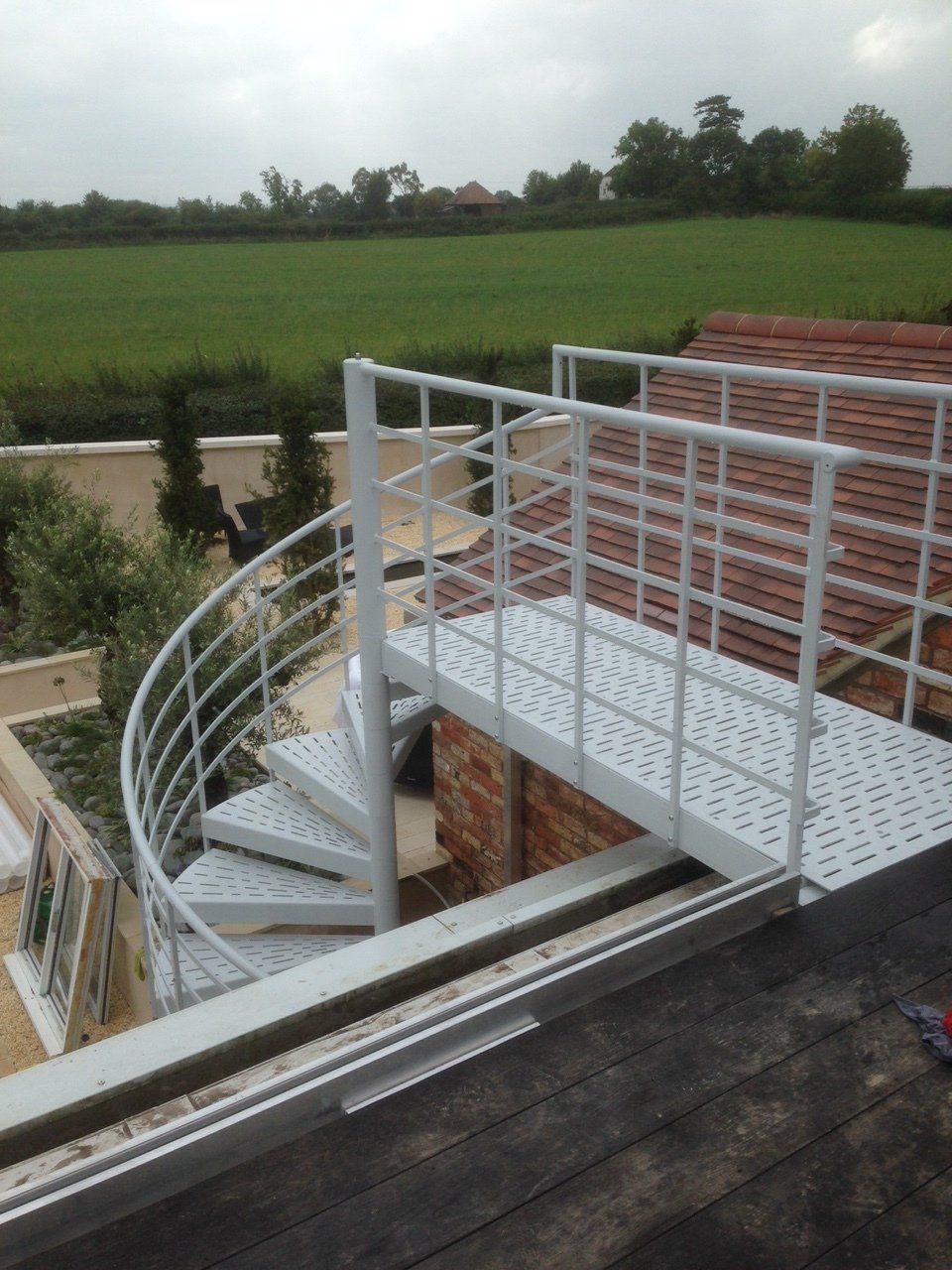 Exterior metal spiral staircase leading to a rooftop landing, painted white.