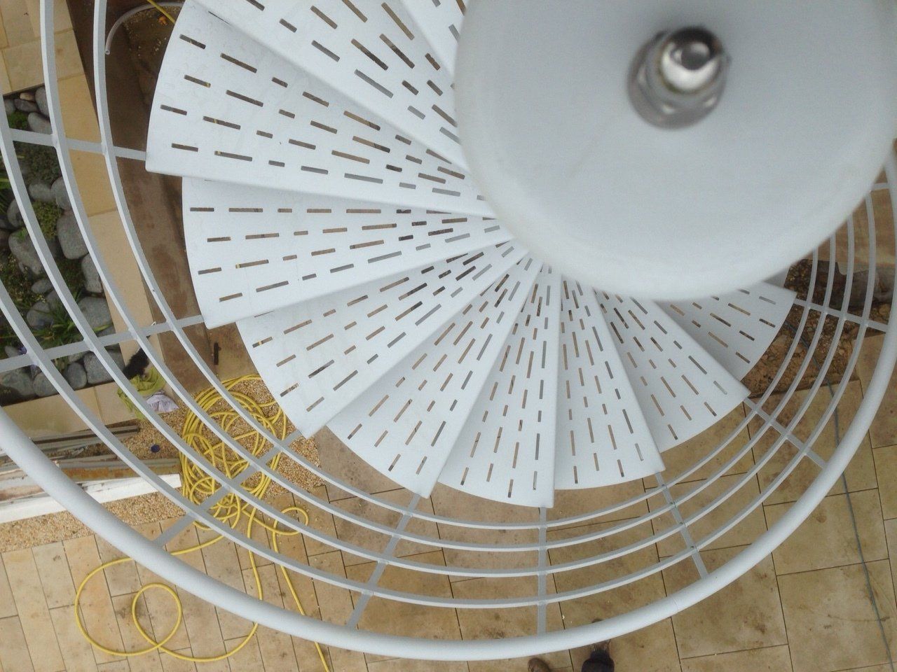 White spiral staircase viewed from above, with perforated steps and metal railing.