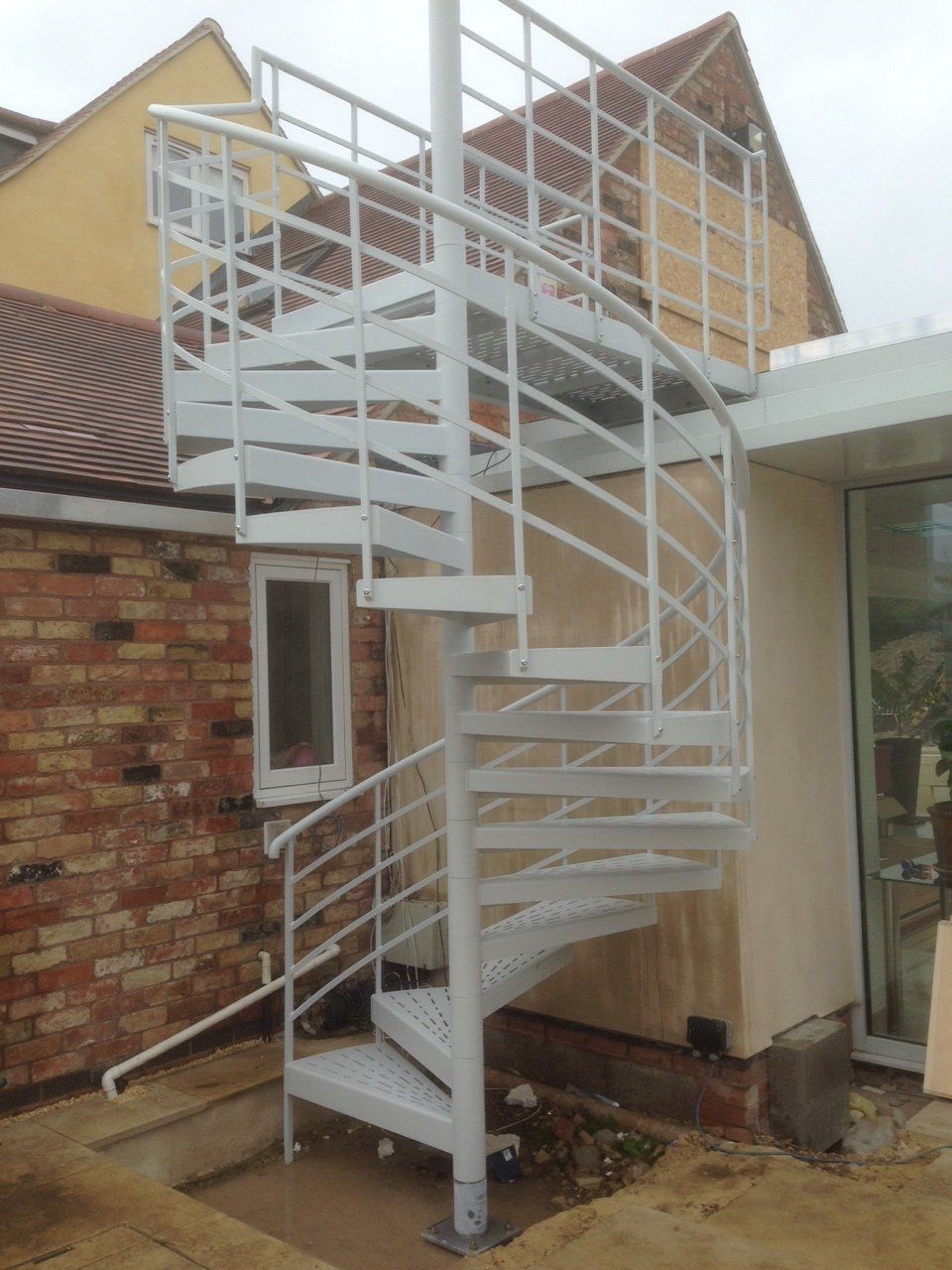 White spiral staircase outside a brick building, leading to a rooftop landing.