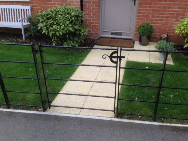 Black metal gate and fence in front yard with a stone path leading to a gray door.