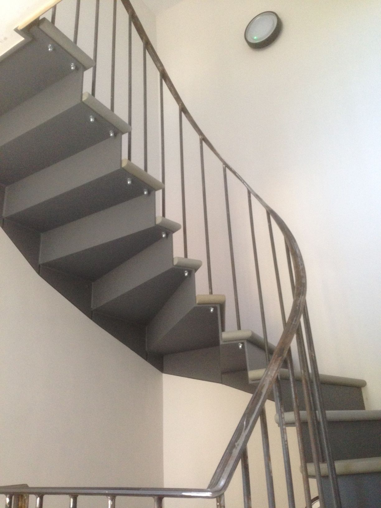 Curving gray staircase with metal railing against a white wall.