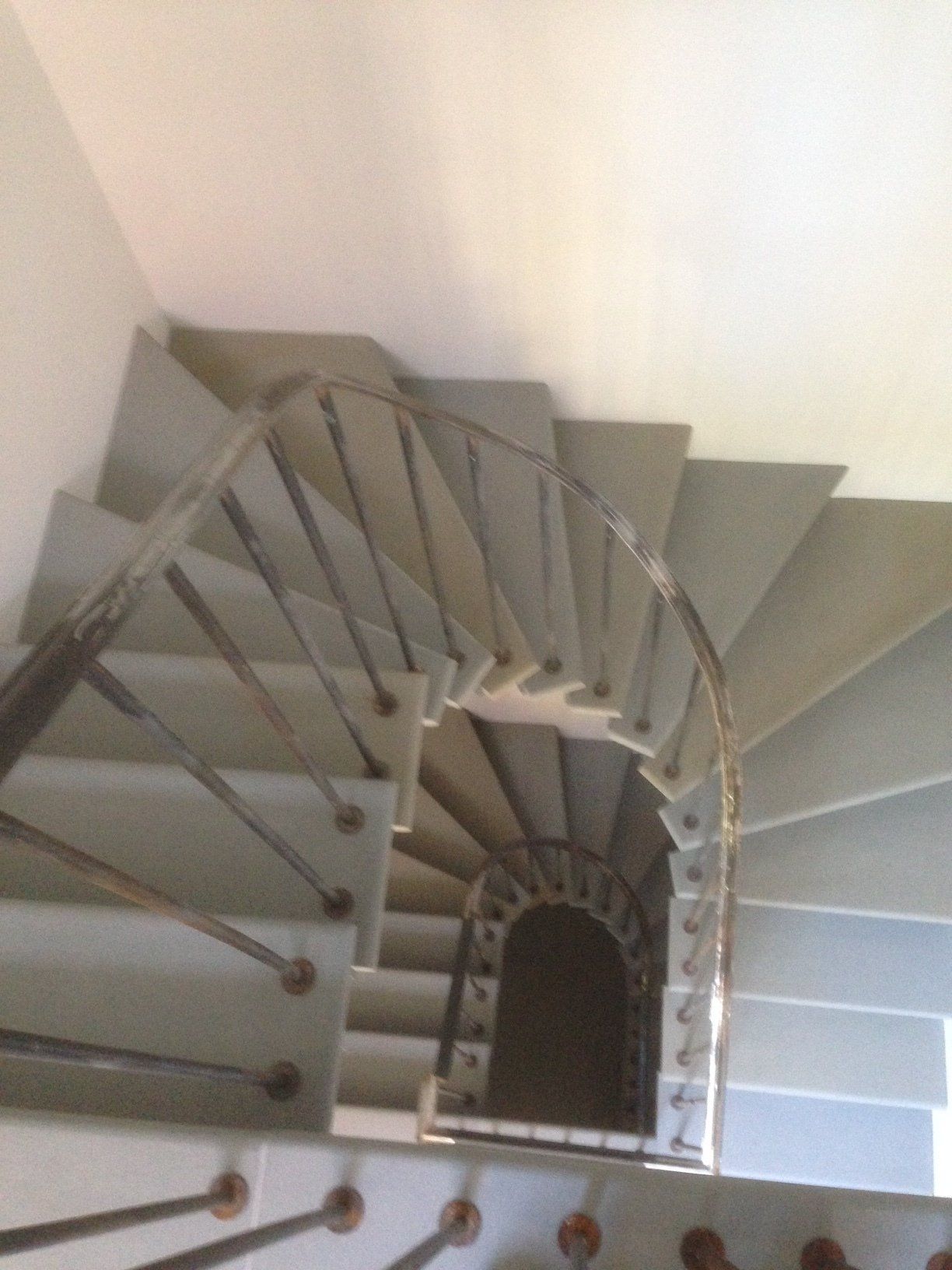 Spiral staircase with light gray steps and dark metal railing, viewed from above.