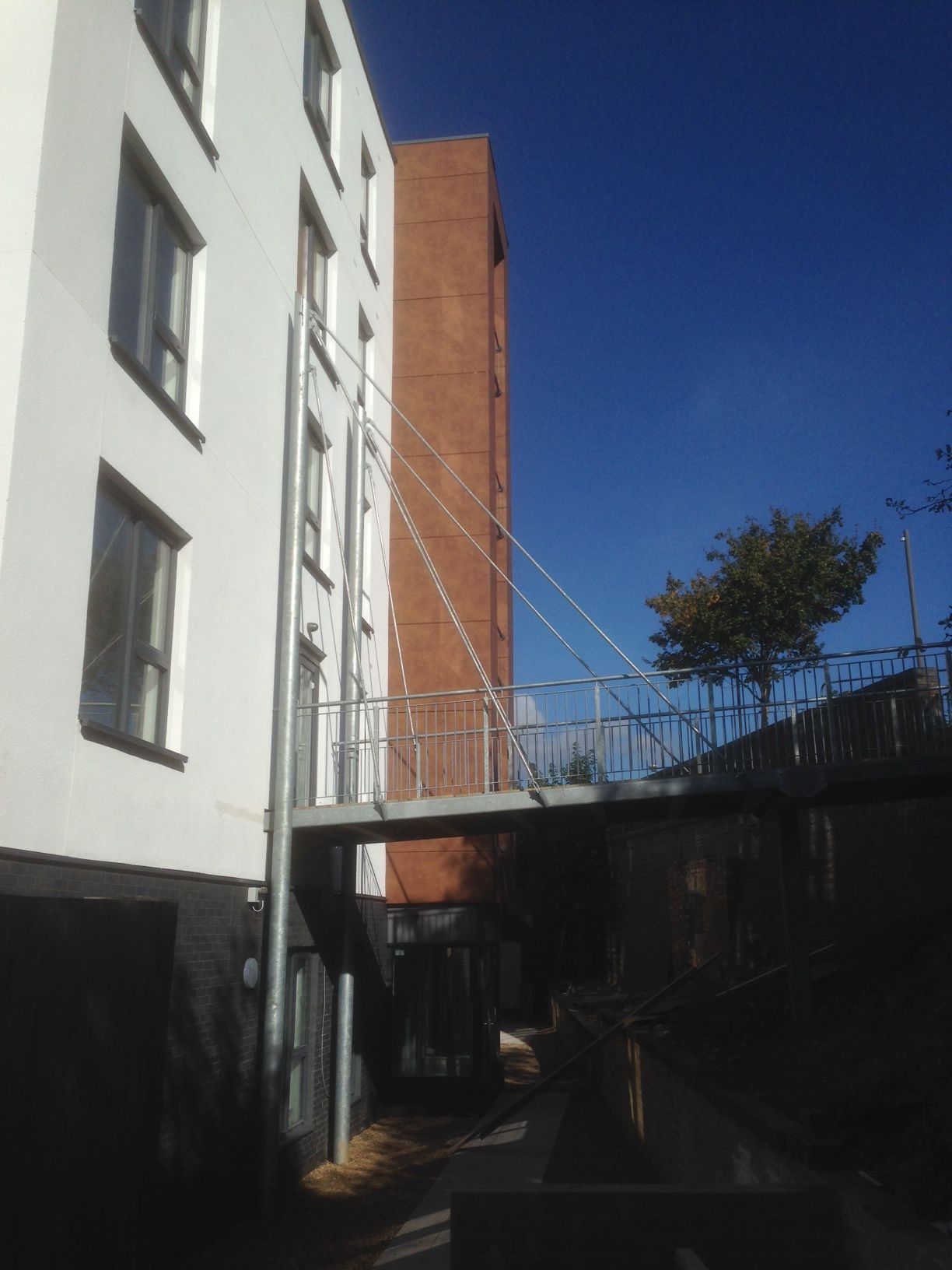 White building with walkway connecting to a red brick building. Blue sky in the background.
