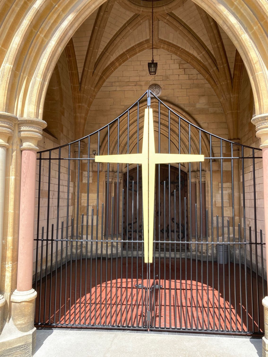 Ornate metal gate with a gold cross, set in a stone archway.