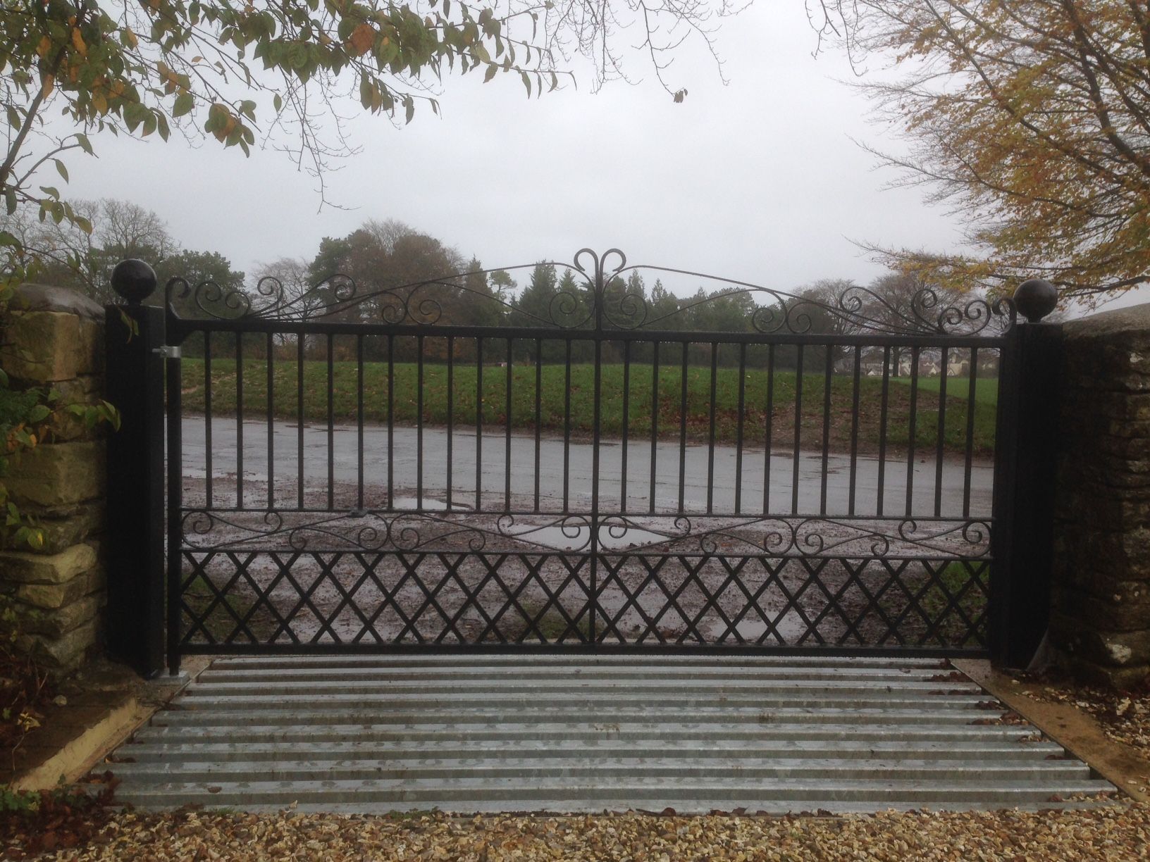 Black wrought iron gate with cow grate in front, leading to a muddy field.