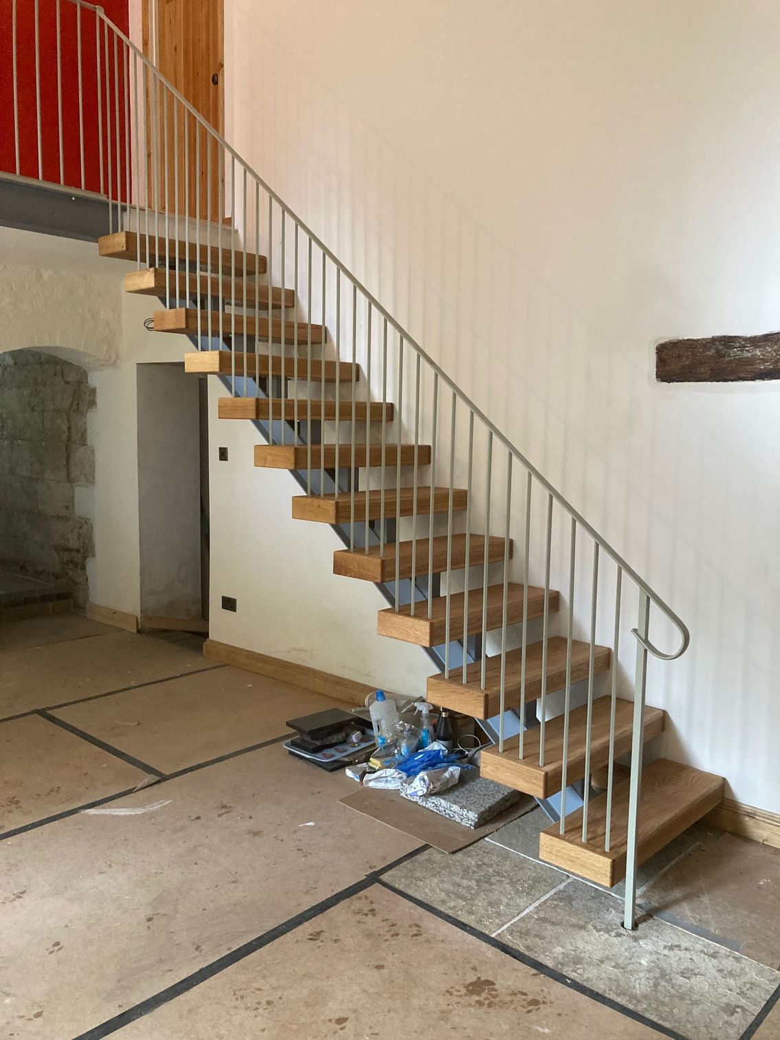 Wooden staircase with metal railing in a room with unfinished flooring and white walls.