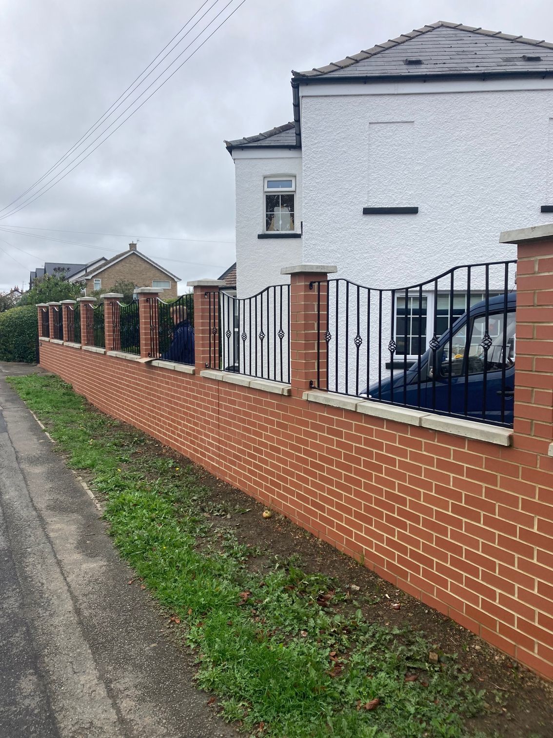 Brick wall with black metal fence and house.