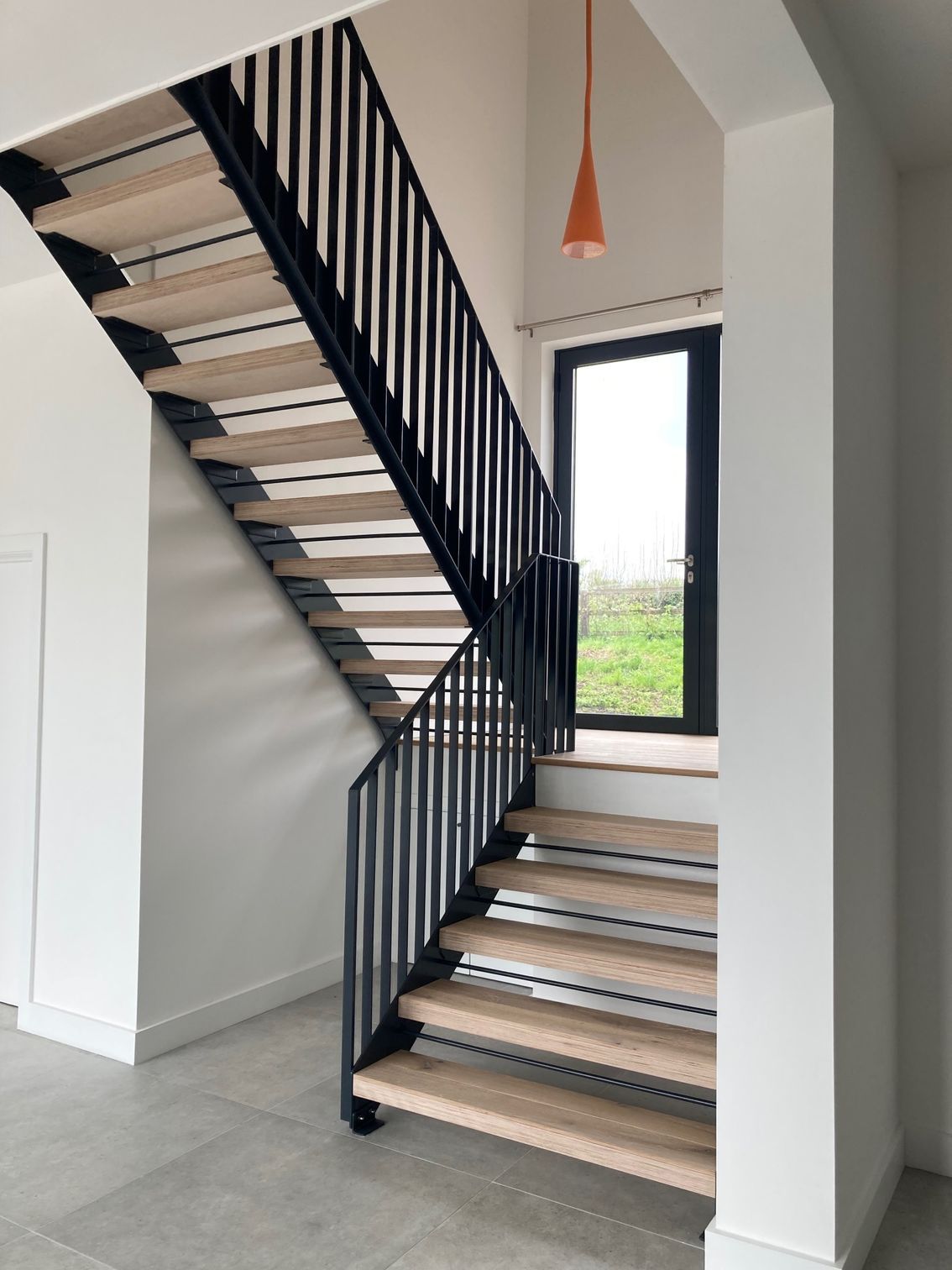 Modern wooden staircase with black metal railings. Orange pendant light hangs above.