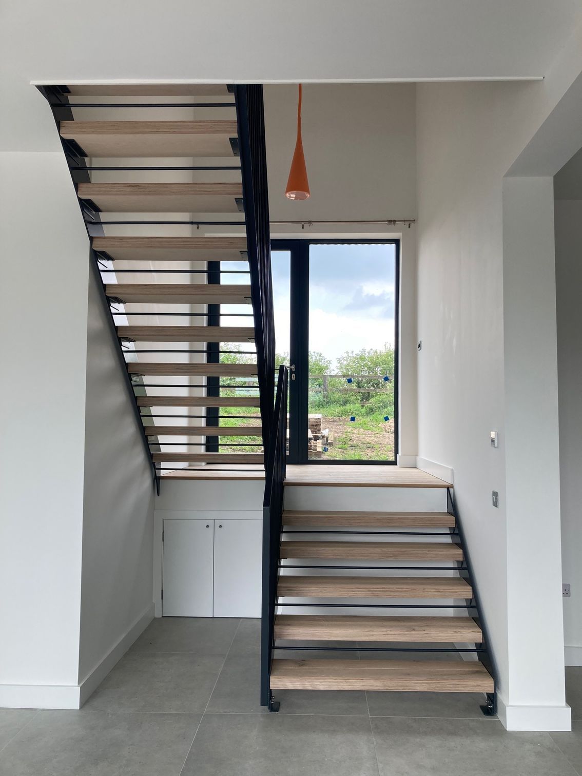 Modern staircase with wooden steps and black metal frame, leading to a doorway and an orange pendant light.