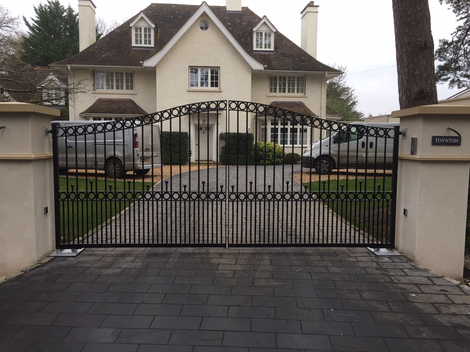 Black metal gate in front of a light-colored house. Two delivery vans are visible behind the gate.