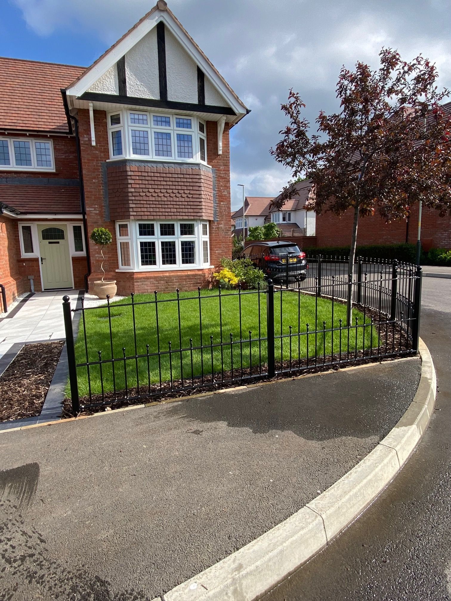 Brick house with black fence, green lawn, paved walkway, and street in front.