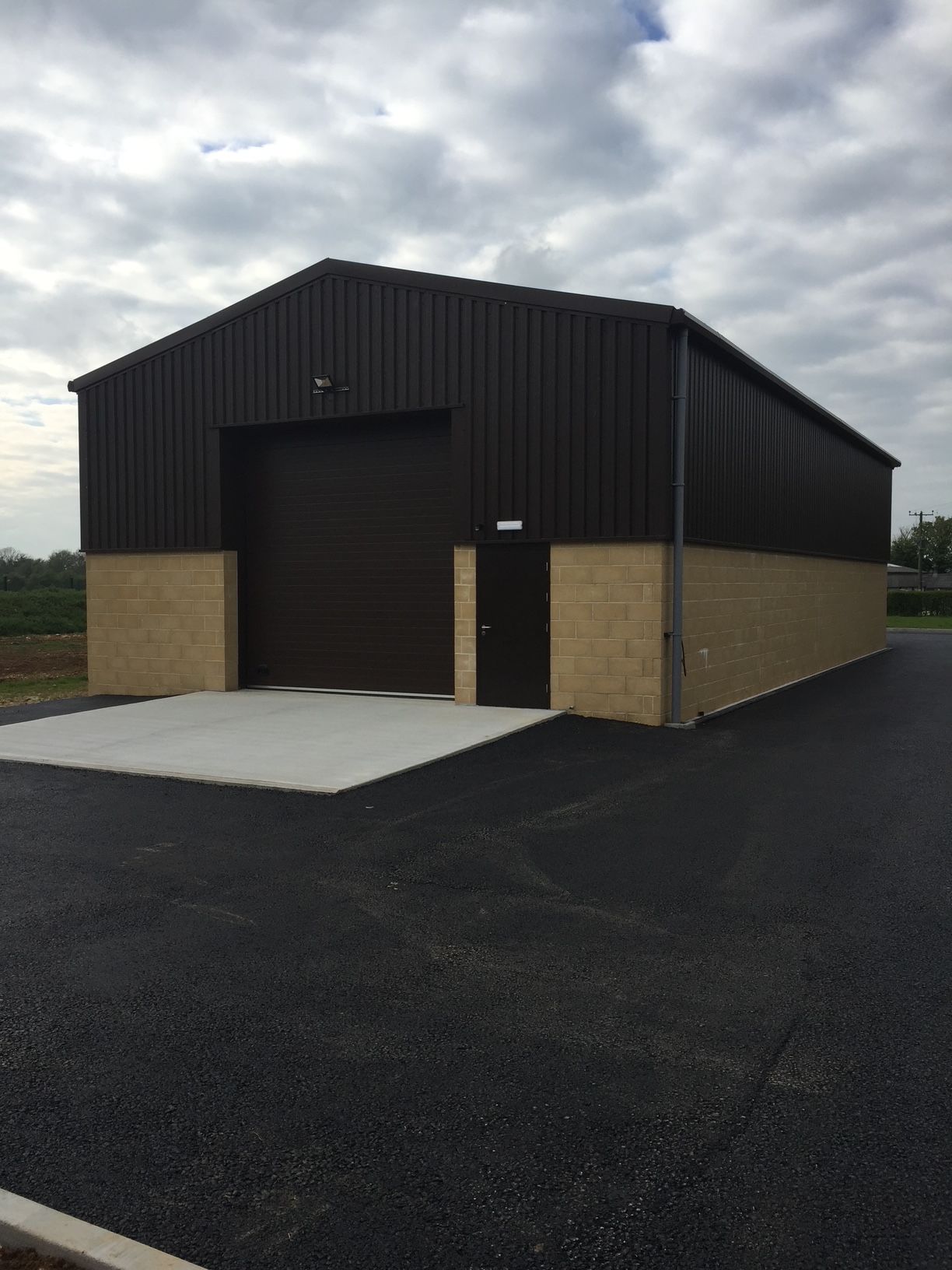 Brown metal warehouse with a tan brick base and a paved driveway.