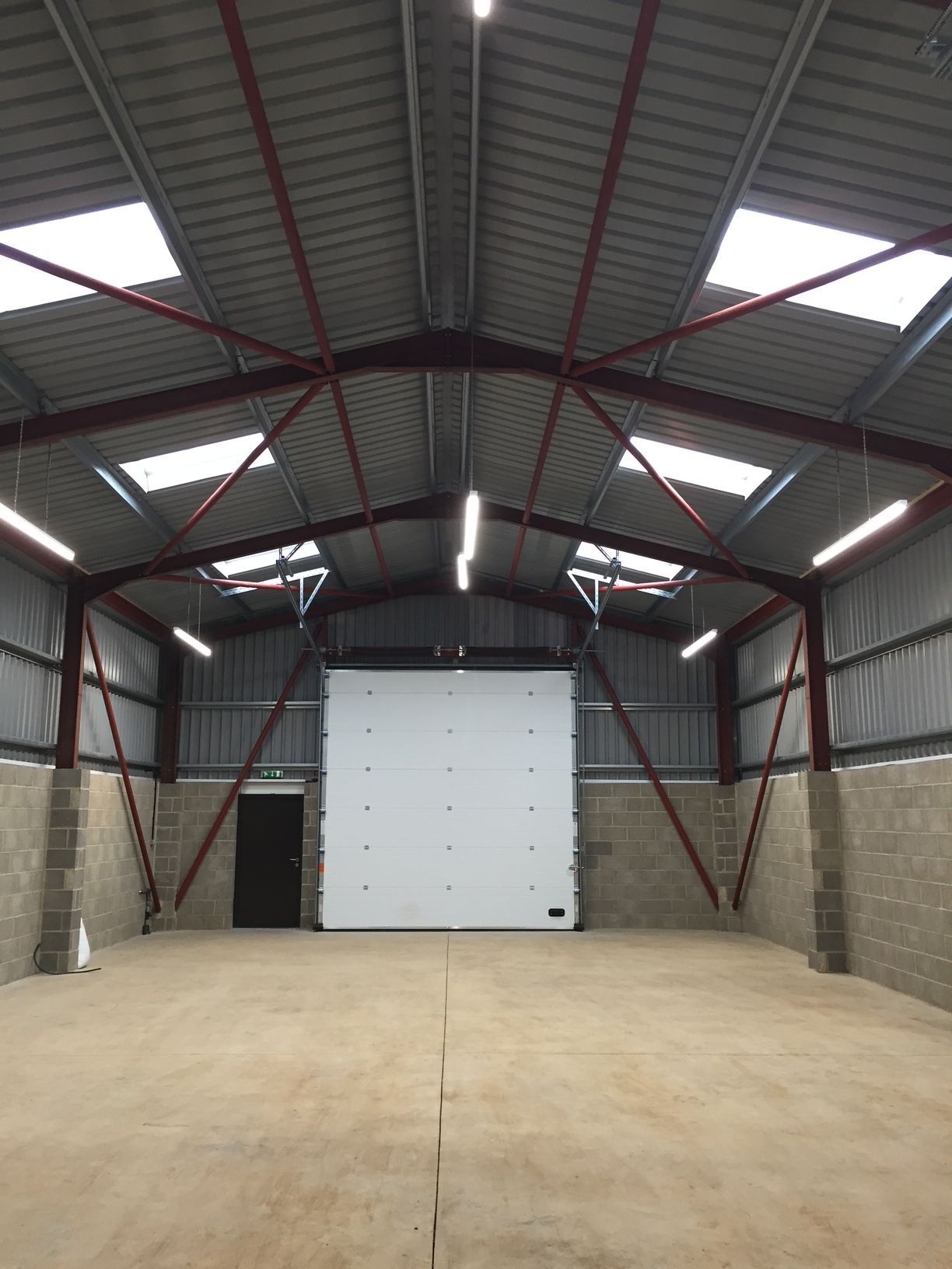 Interior of a warehouse with a concrete floor, large white door, and metal roof.