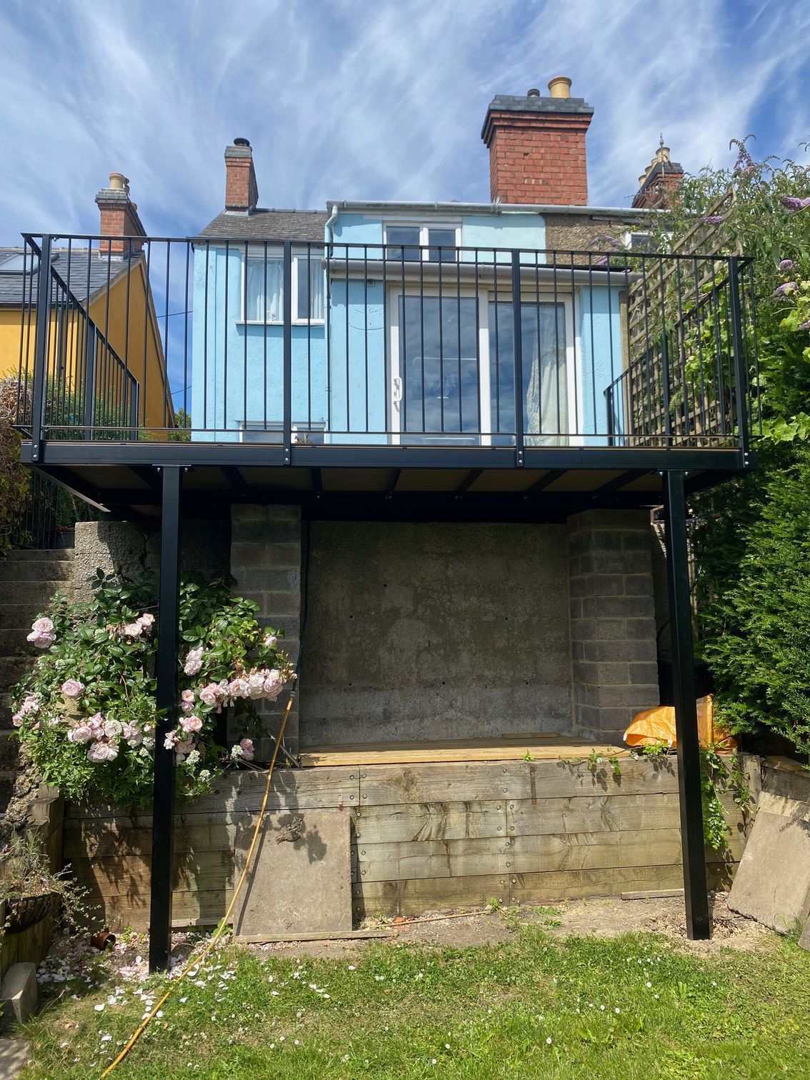 Black metal deck with railings and blue house in background.