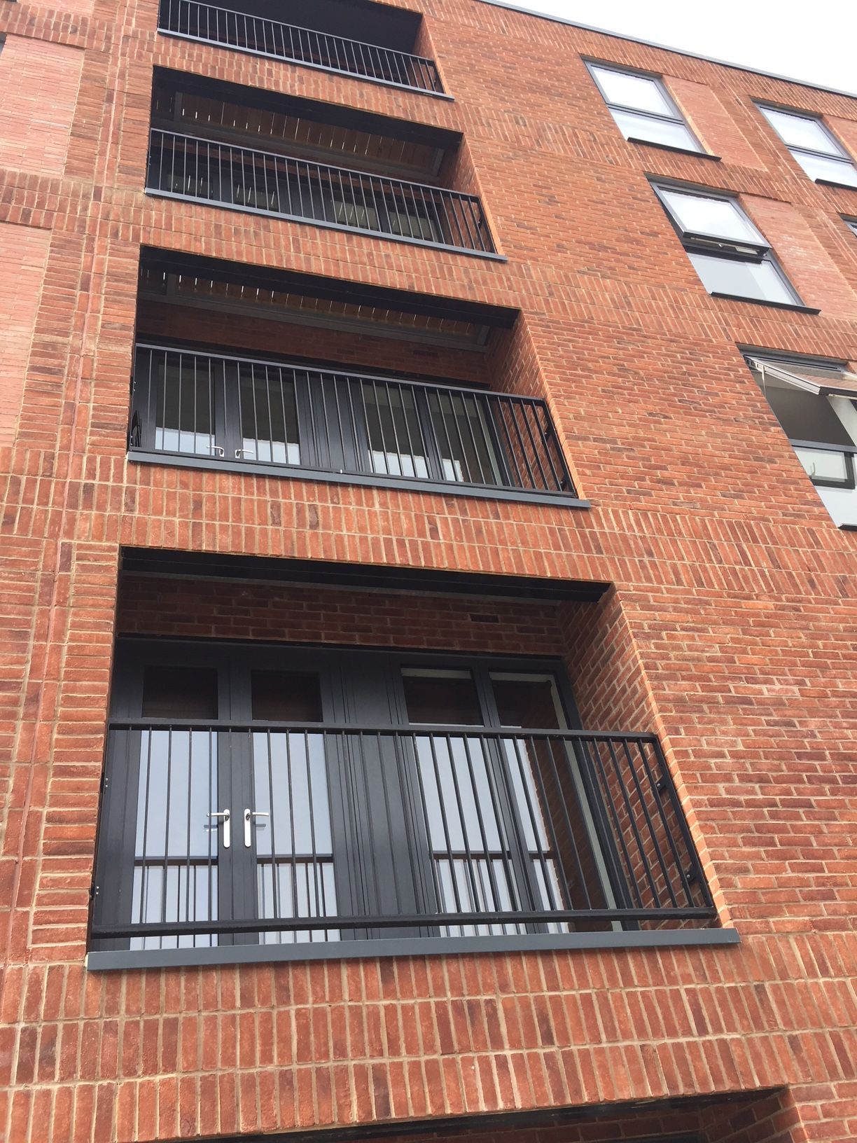 Red brick apartment building with black balconies and windows.