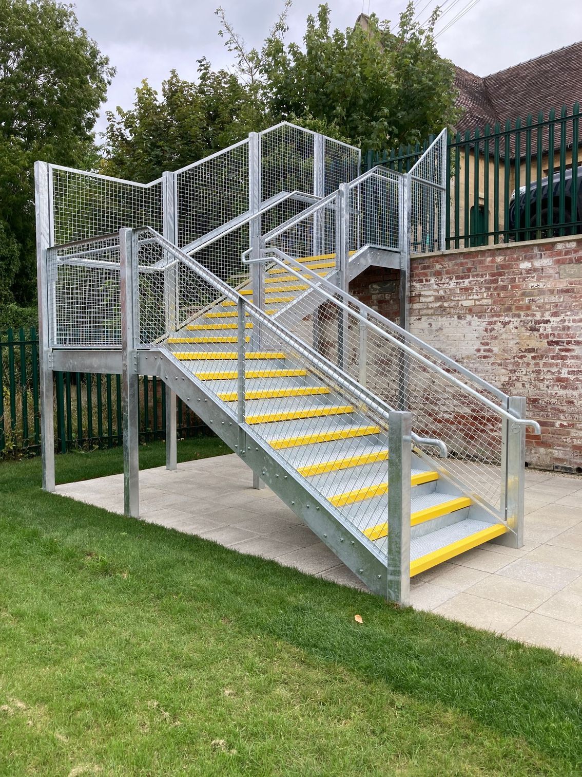 Metal staircase with yellow step edges, concrete base, and green lawn.