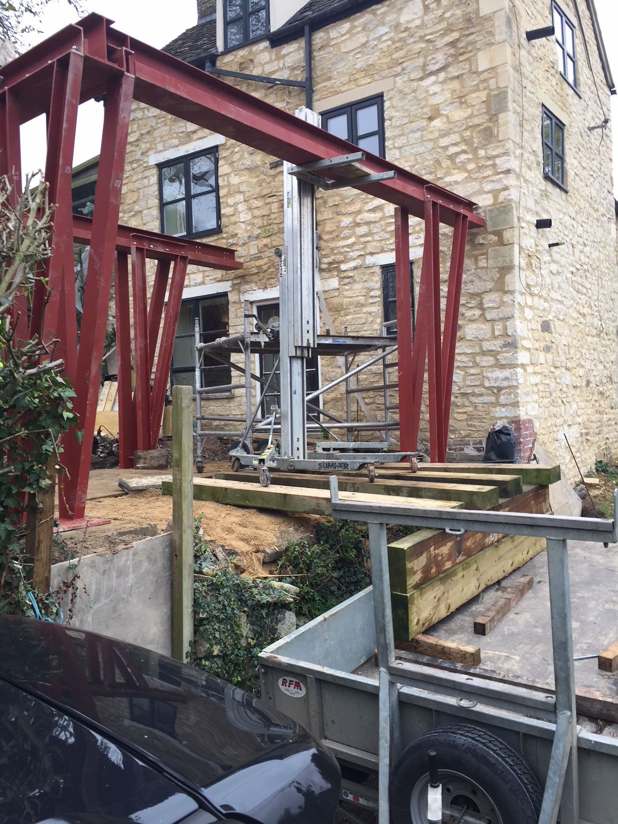 Red steel frame construction on a stone building. Scaffold and trailer in the foreground.