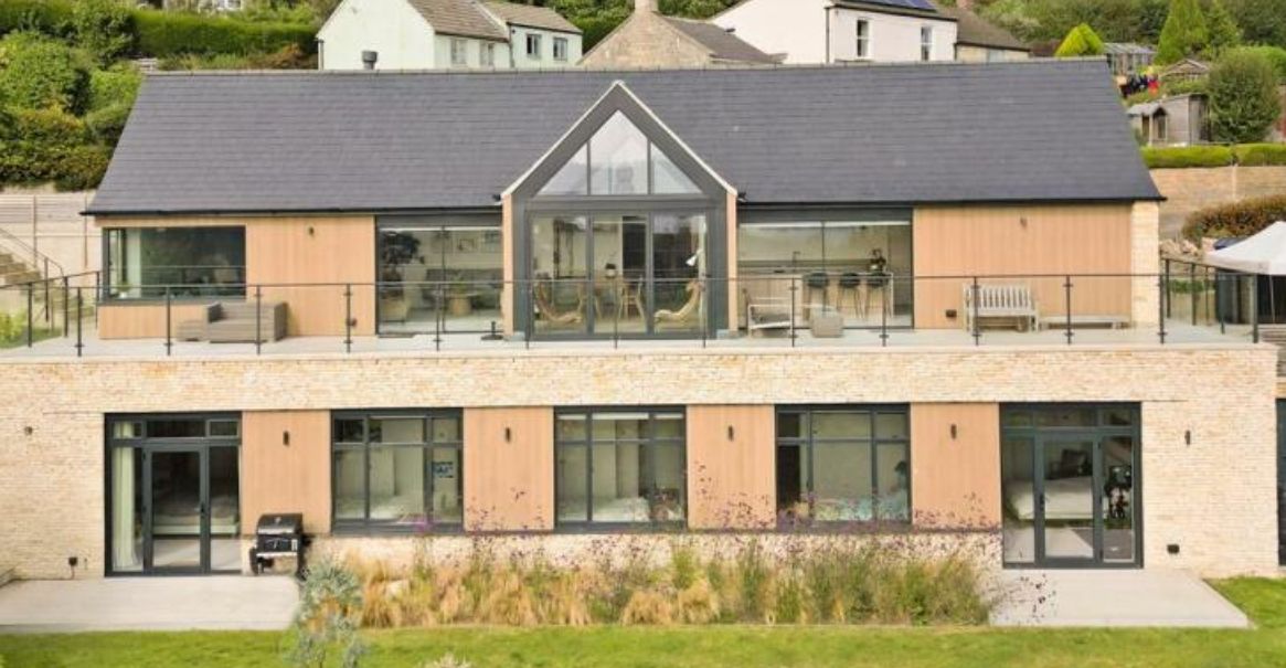 Modern two-story house with a flat roof, large windows, and a glass-paneled gabled section. Set on a hill.