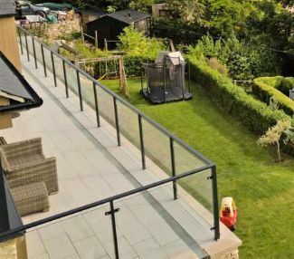Patio with glass railing, wicker furniture, and a backyard with trampoline and swing set.