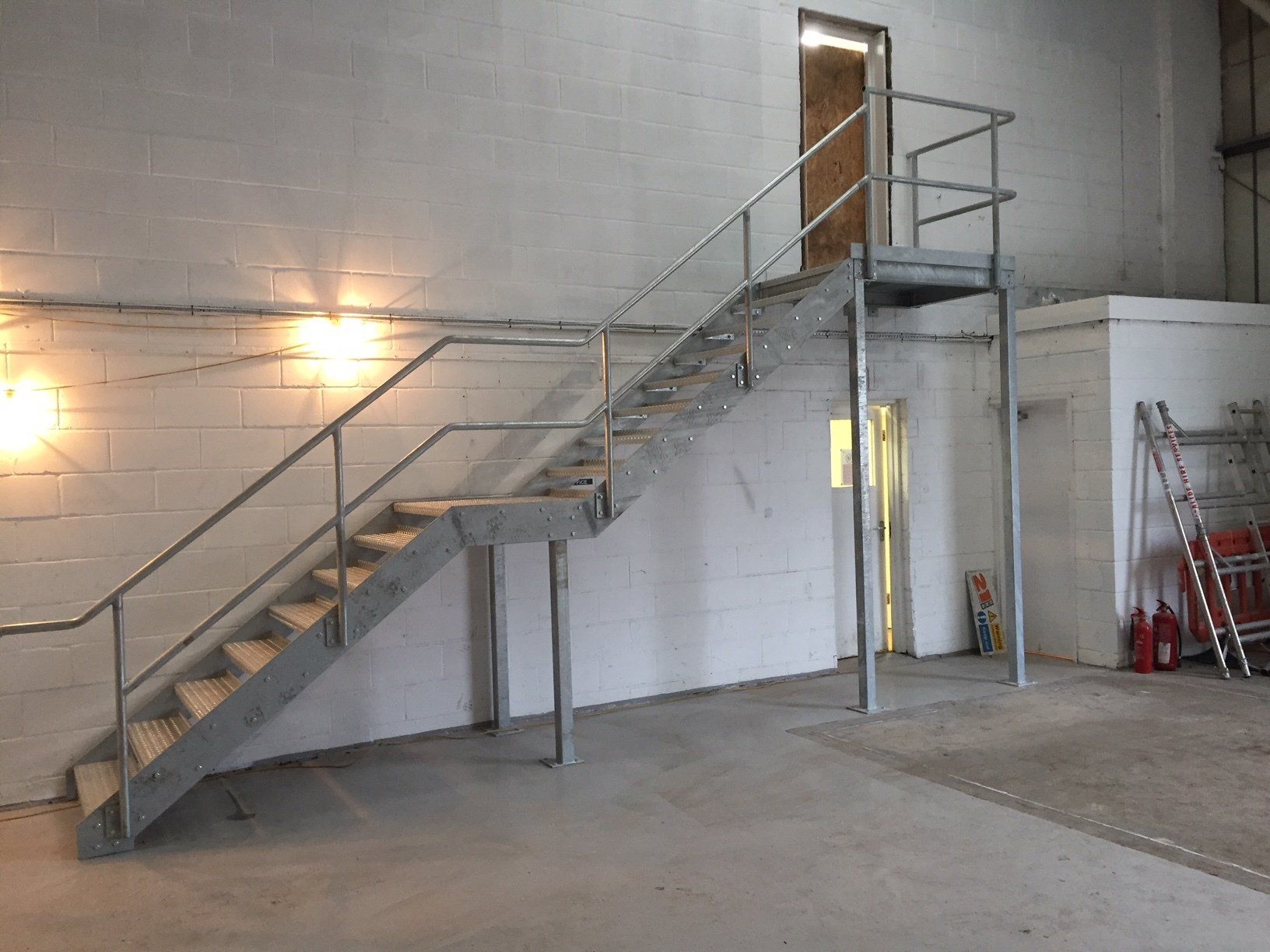 Metal staircase with handrails in an industrial setting, leading to a doorway.