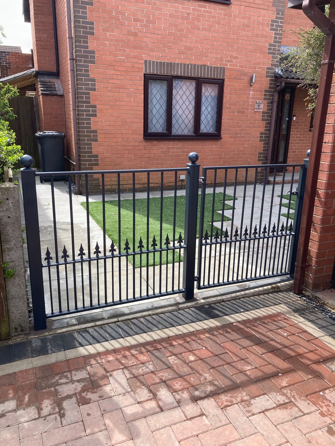 Black wrought-iron gate in front of a brick house with a small lawn.