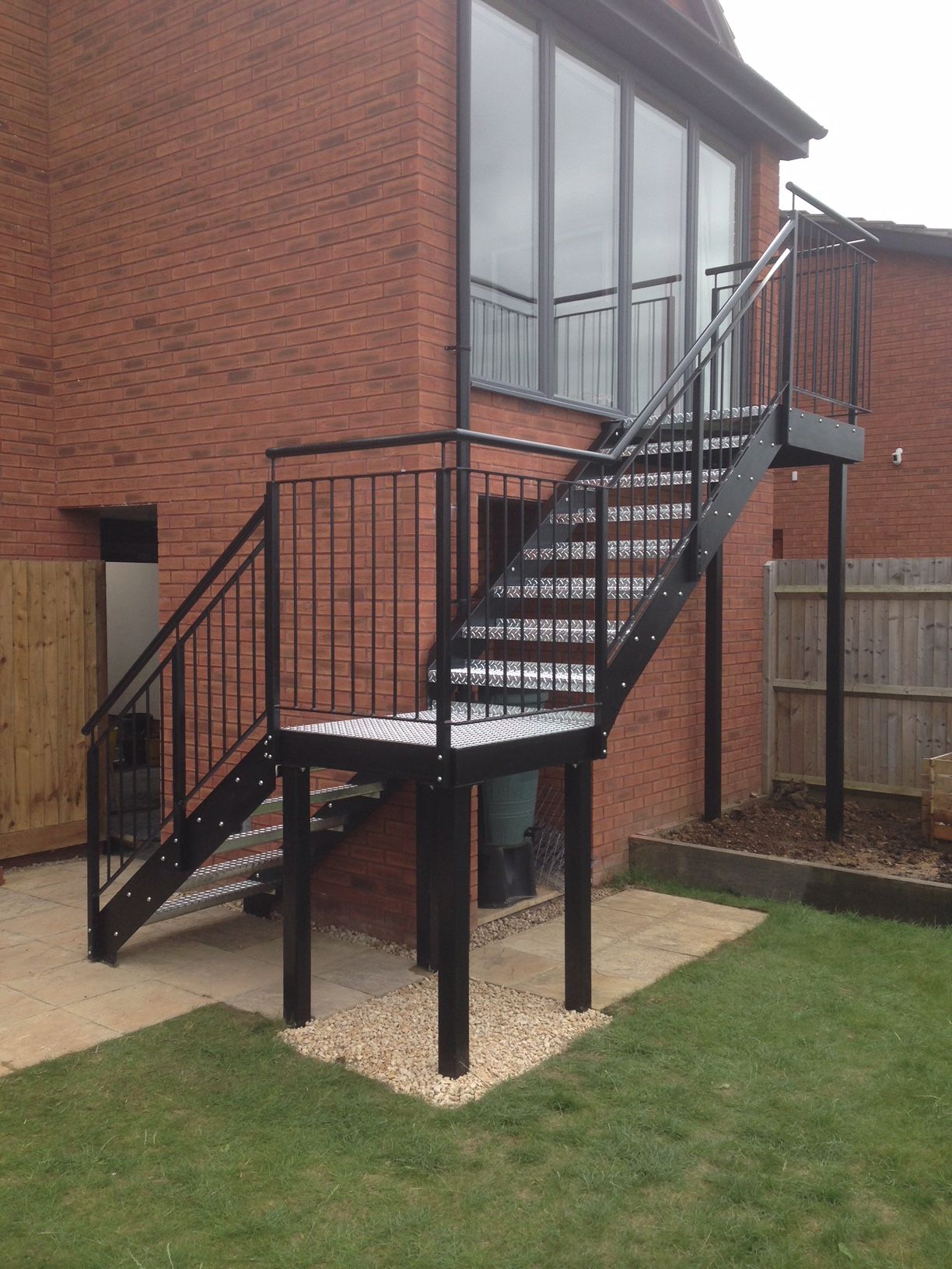 Black metal exterior staircase attached to a brick building. The stairs lead to a platform and upper level.