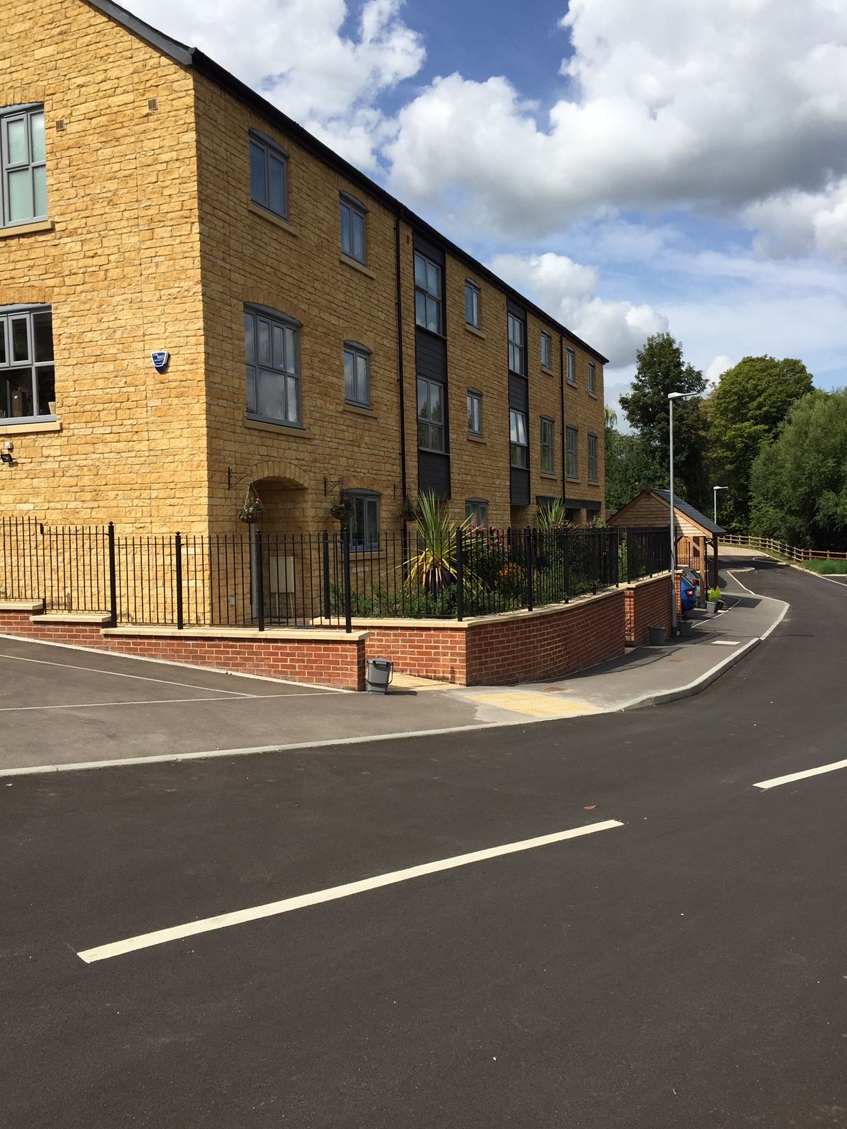 Yellow brick apartment building on a curve, black asphalt road, blue sky with clouds.