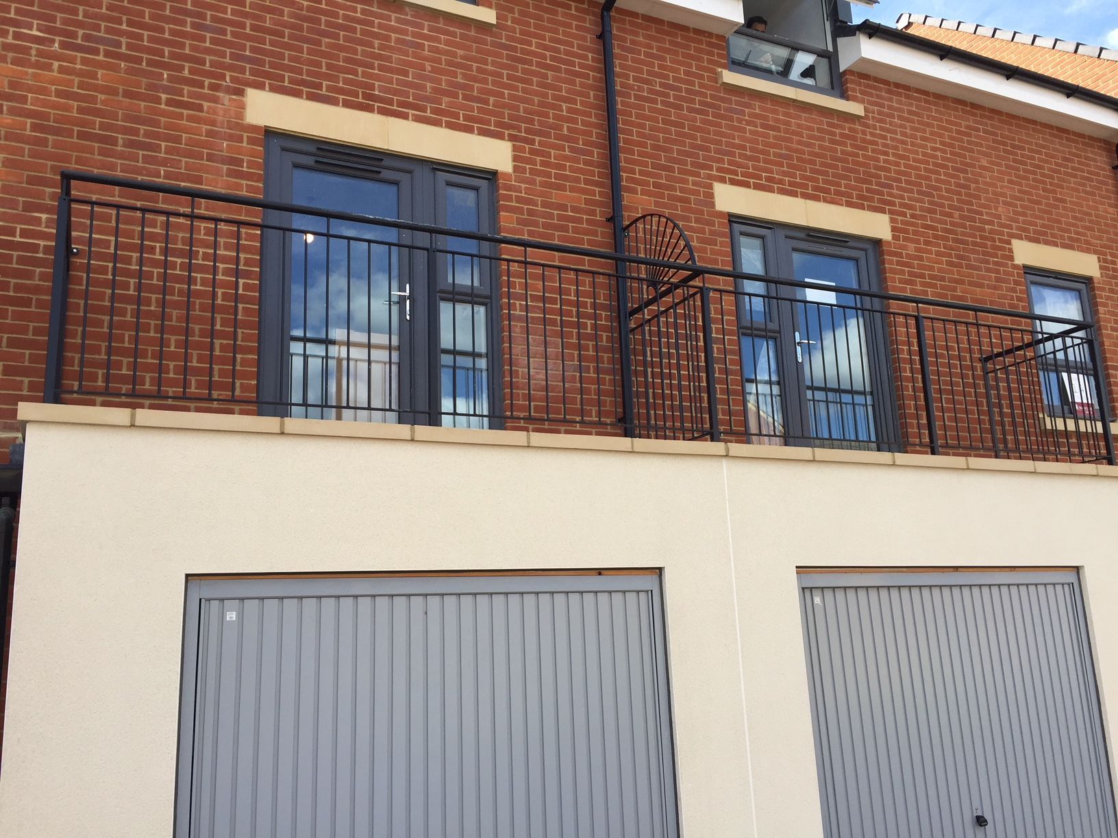 Two-story brick building with grey garage doors and balconies with black railings.