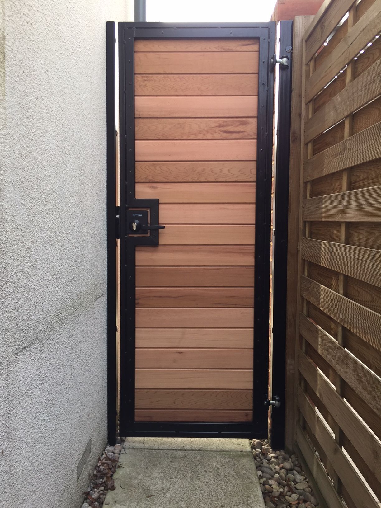 Wooden gate with horizontal planks, black metal frame, and a latch.