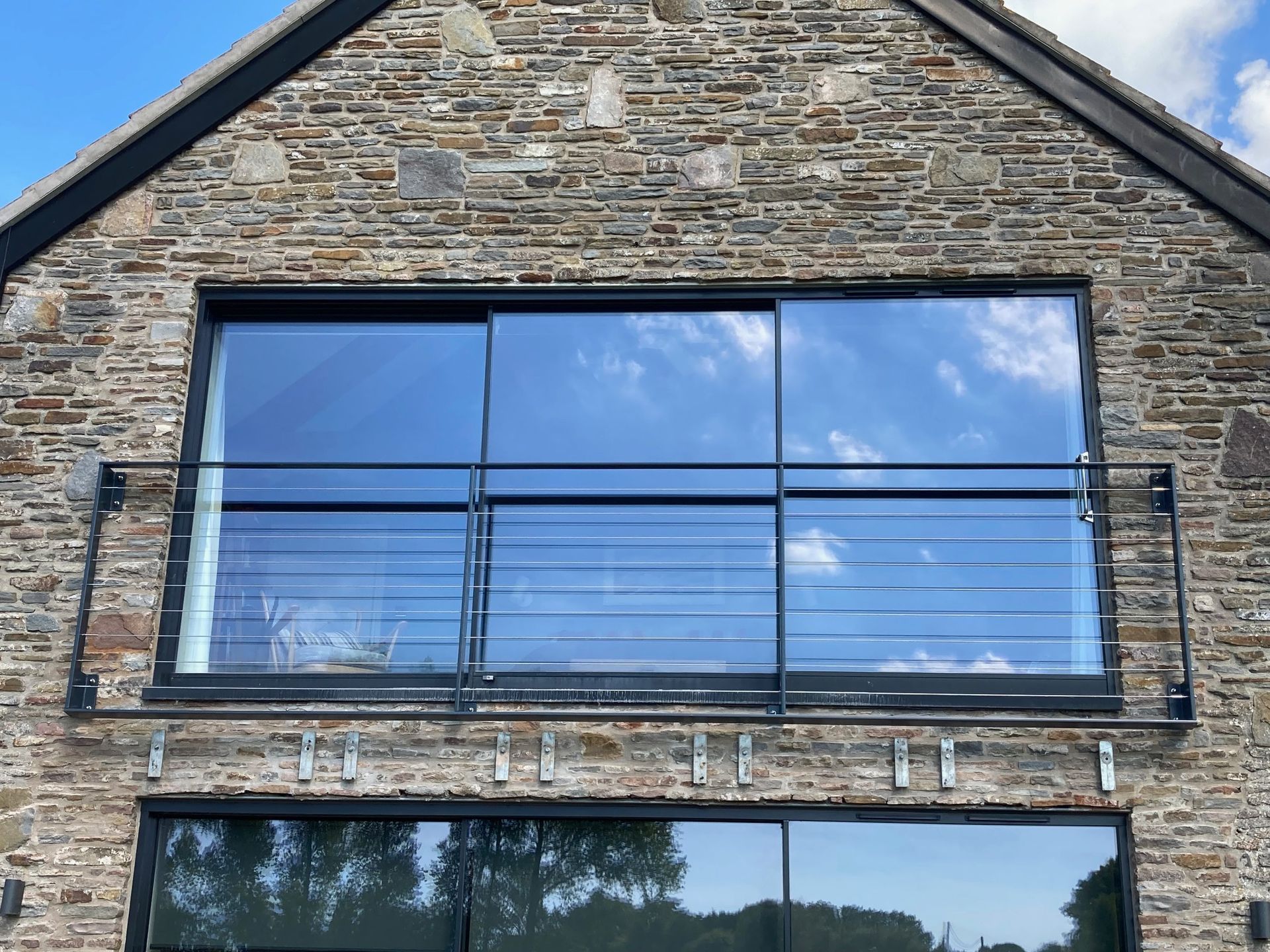 Stone building with a large black-framed sliding glass door and balcony. Reflective sky.