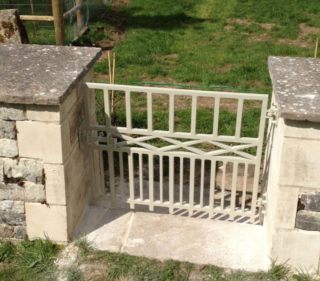 Beige metal gate between stone pillars, leading to a grassy area.