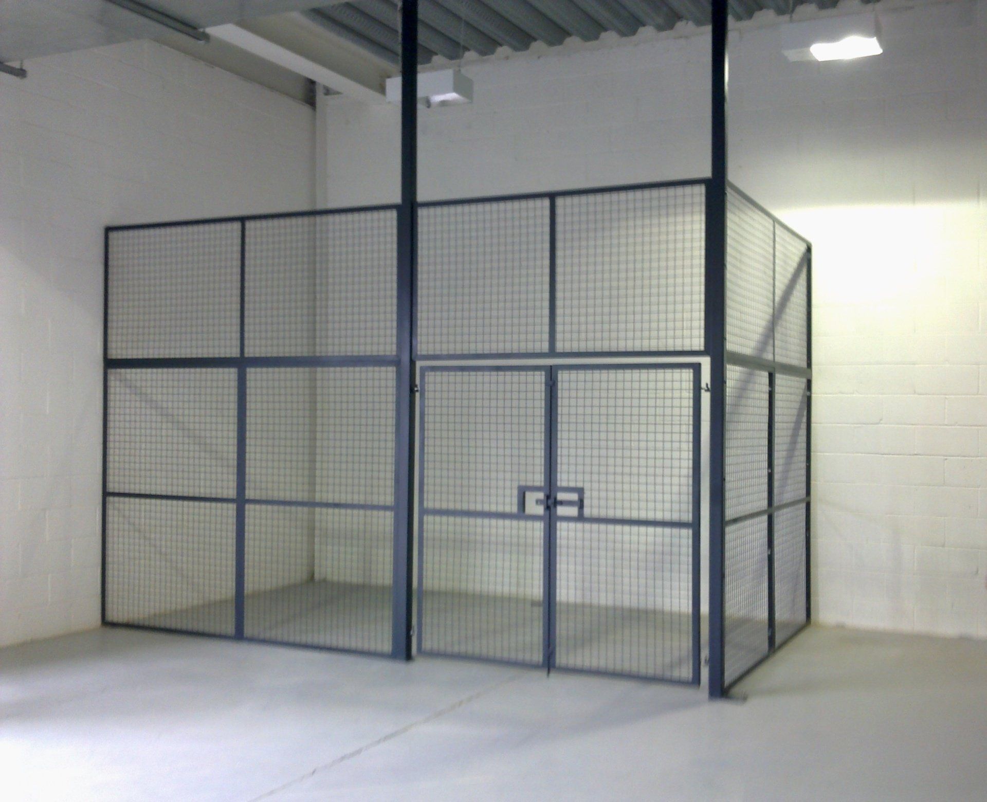 Metal mesh security cage inside a large warehouse. Includes a door and vertical supports.