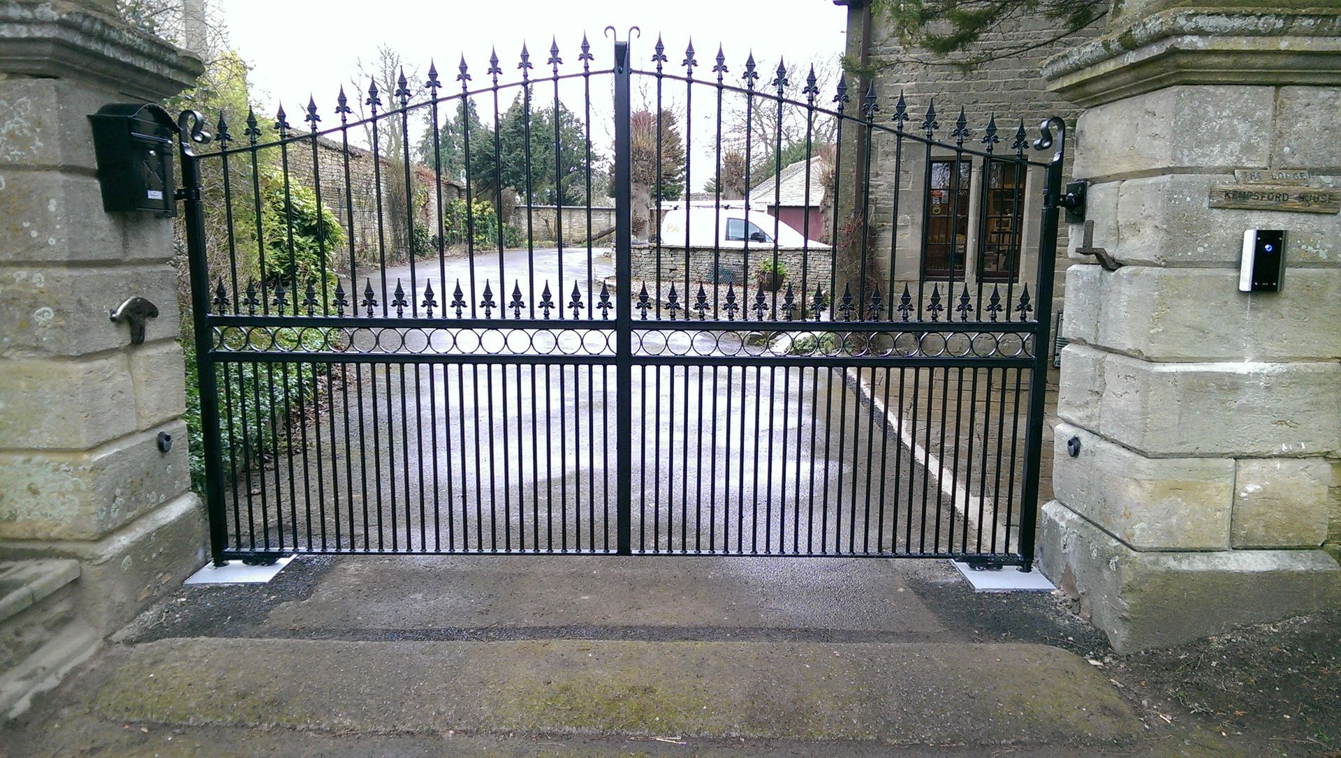 Black wrought iron gates between stone pillars.