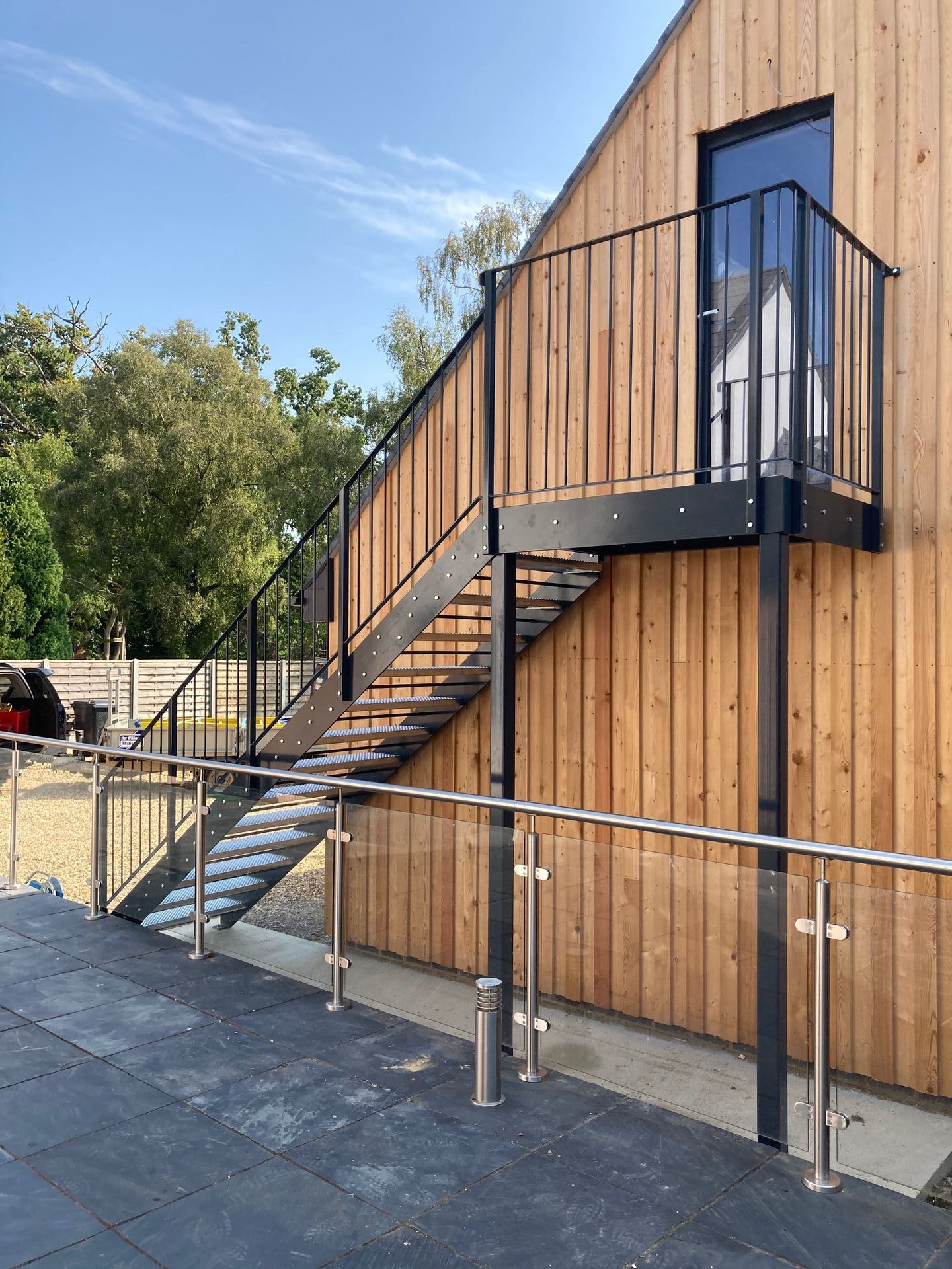 Exterior staircase attached to a wooden building with black railings and glass panels.