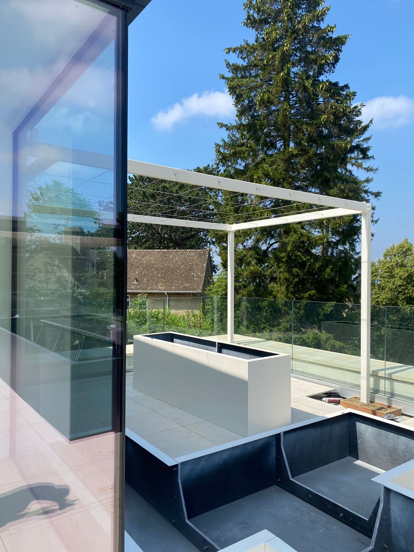 Modern outdoor space with white pergola, light gray planter, and glass wall.