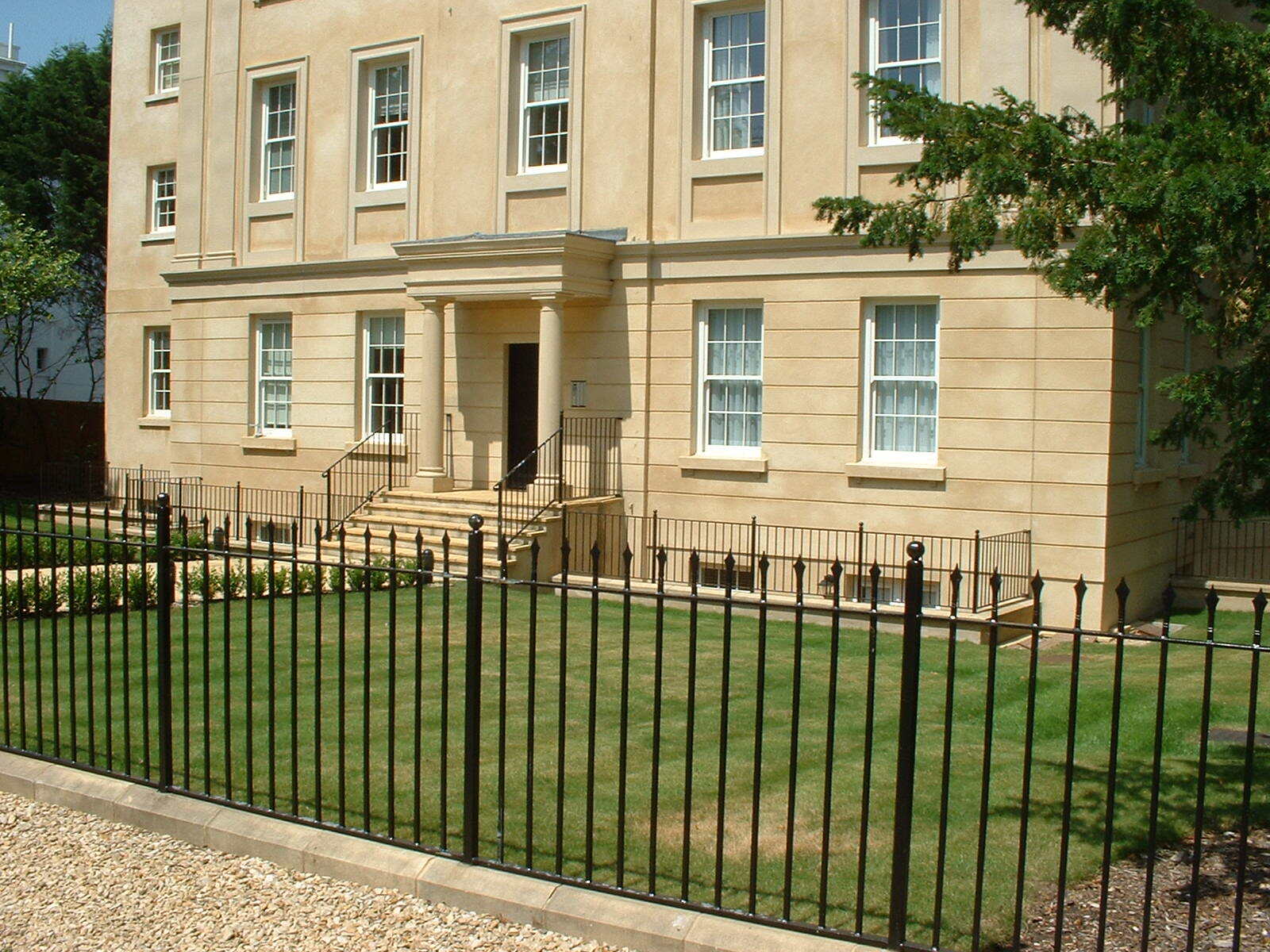 Beige stone building with a black wrought-iron fence and a green lawn.