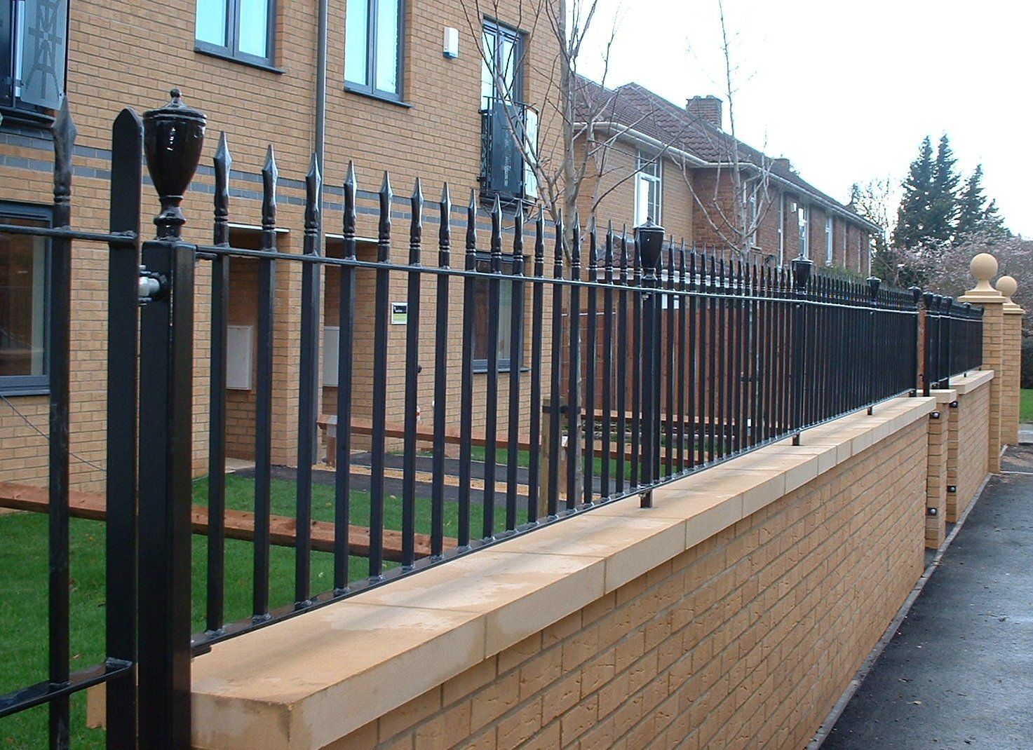 Black wrought iron fence with spikes atop a brick wall in front of a building.